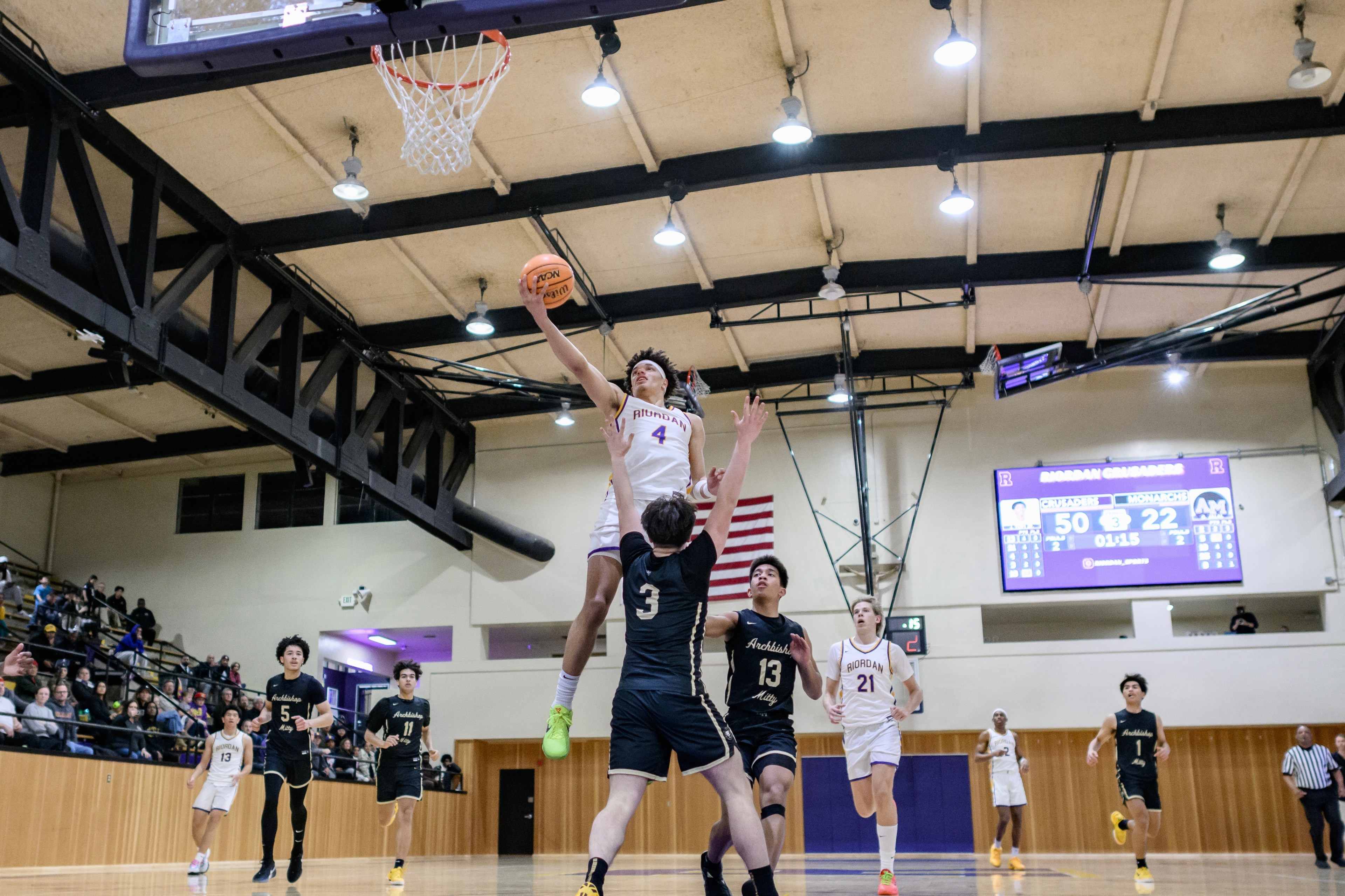 A basketball player in a white uniform leaps towards the hoop to score, while players in black attempt to block him. The scoreboard reads 50-22.