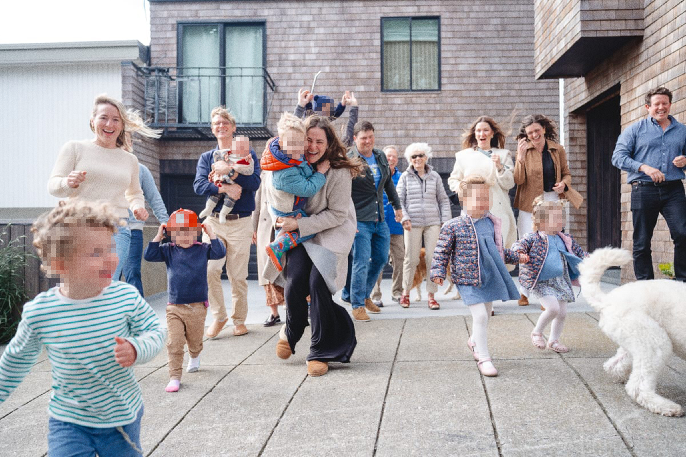 A joyful group of adults and children, some with pixelated faces, are outside a house, happily running and interacting, with a dog in the foreground.