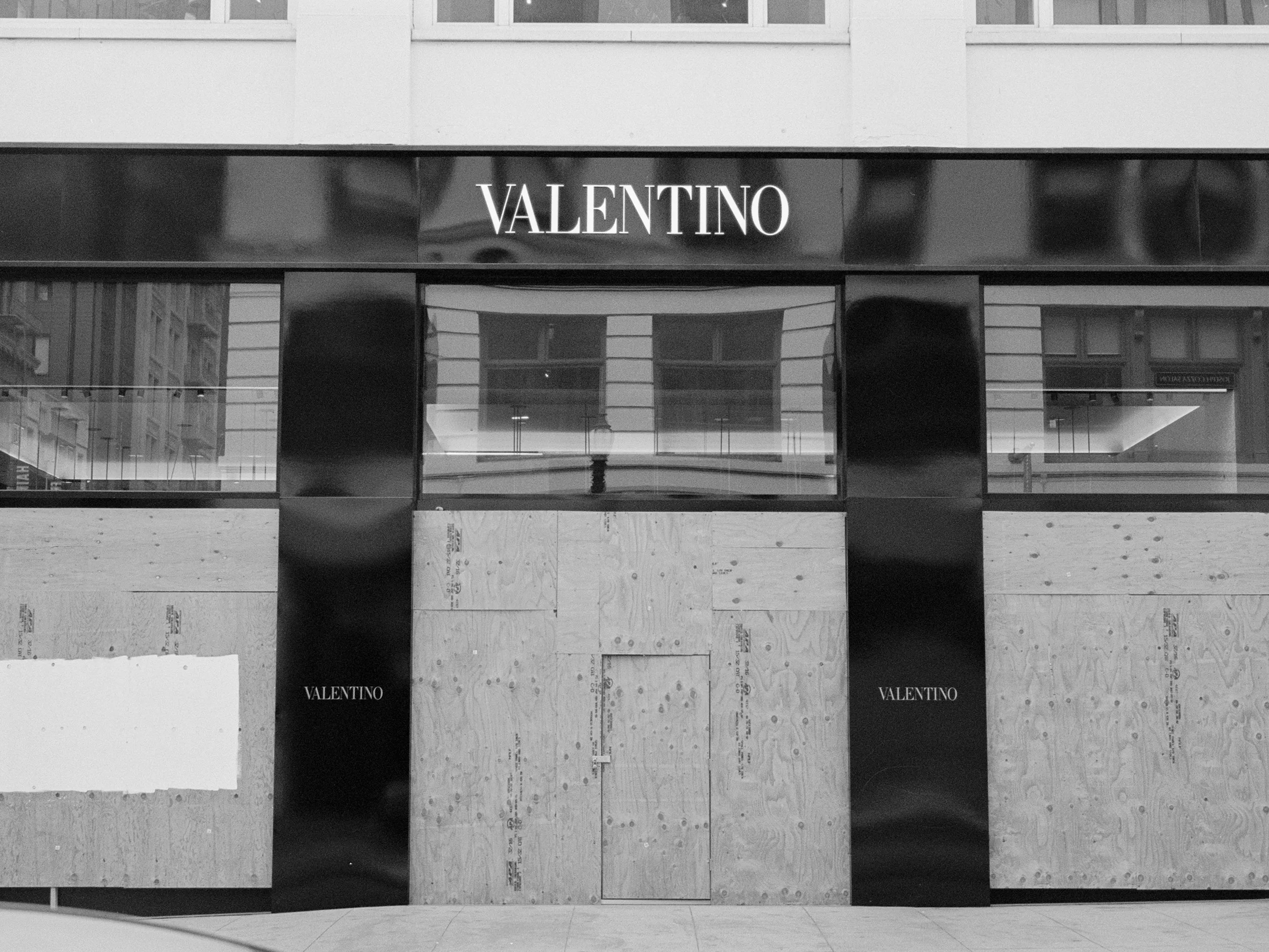 The image shows a Valentino store with its entrance boarded up with plywood. The store's name is displayed in large letters above the doors.