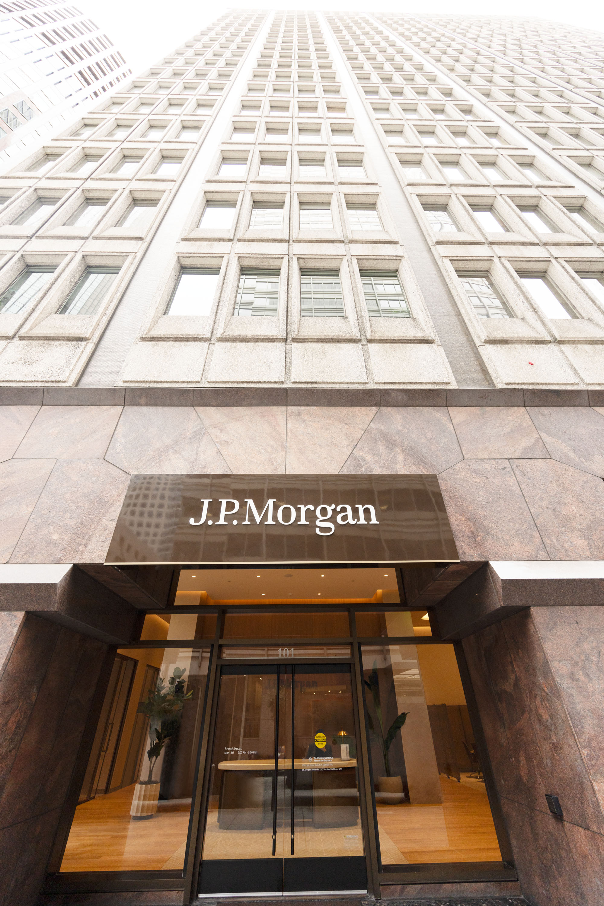 JPMorganChase's Financial Center at 111 Pine St. A tall building with the perspective looking up from the entrance titled with the J.P.Morgan sign.