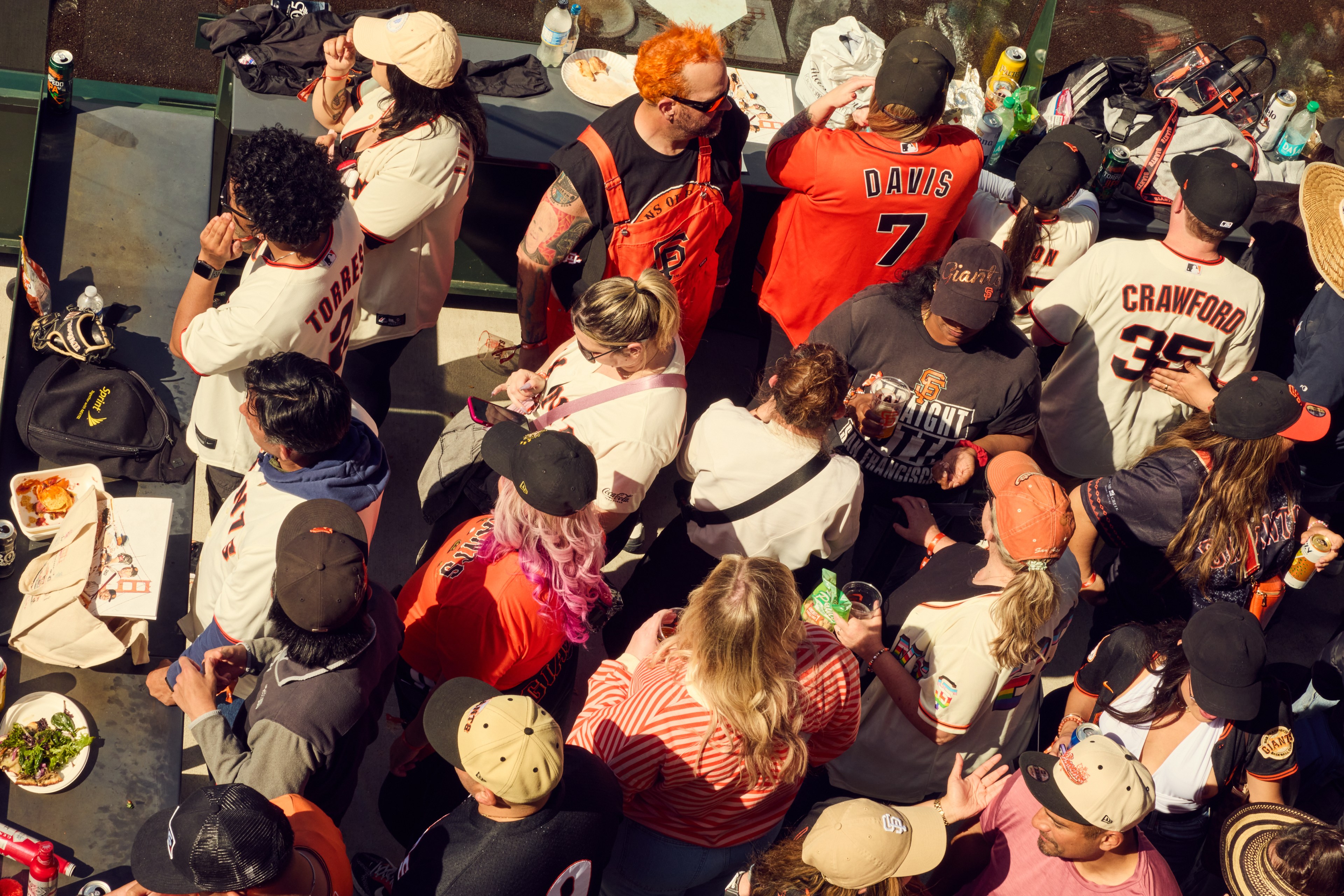 A group of people wearing San Francisco Giants gear, including jerseys and caps, gather around tables with food and drinks at an outdoor event.