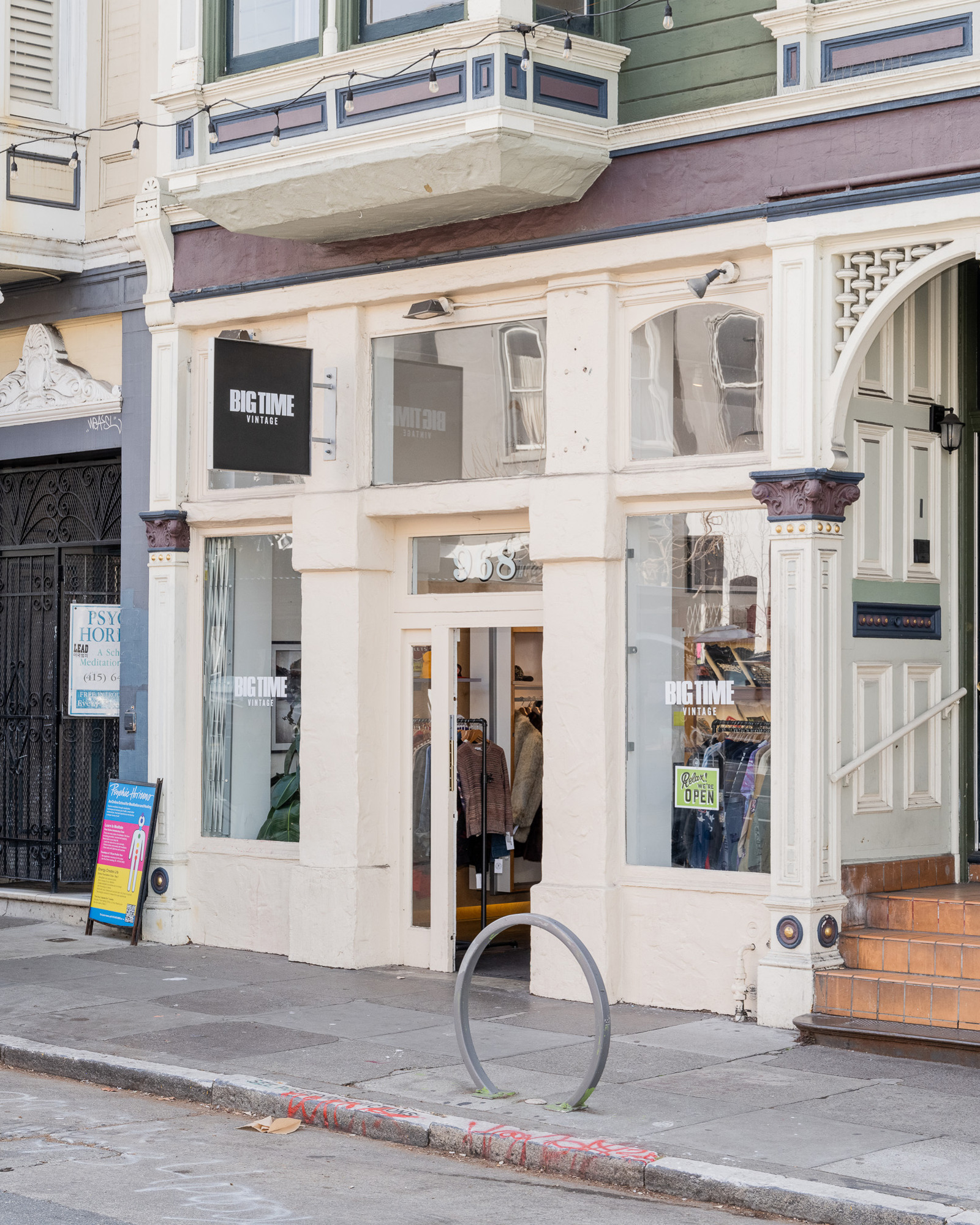 The image shows the entrance of a vintage clothing store named &quot;Big Time Vintage.&quot; It's housed in a classic building with an open door showing racks of clothes.