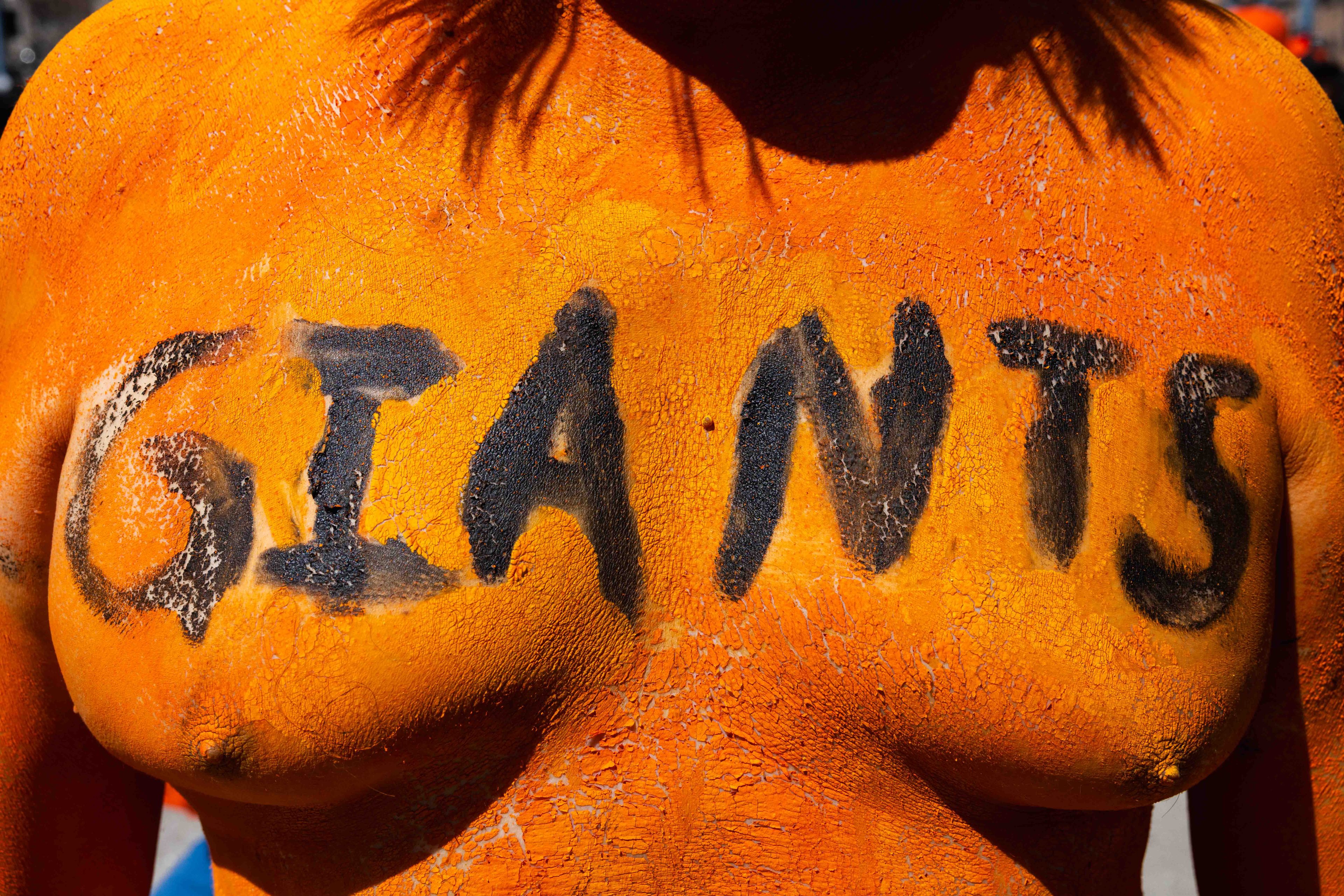 A person's chest is painted bright orange with the word &quot;GIANTS&quot; in bold black letters across it. The paint appears cracked and textured.