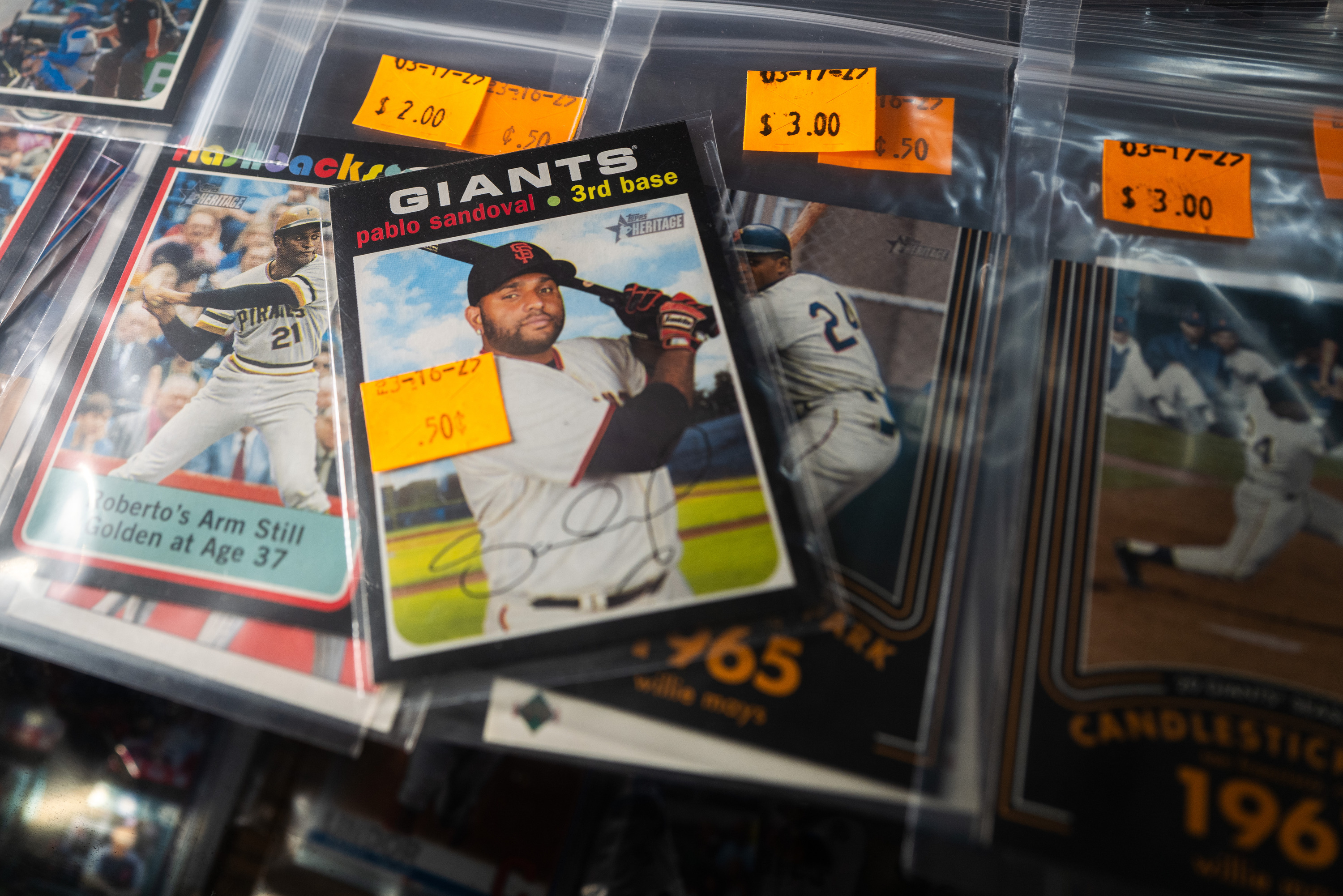 The image shows a collection of baseball cards in plastic sleeves with orange price tags, featuring various players and their names, teams, and playing stats.