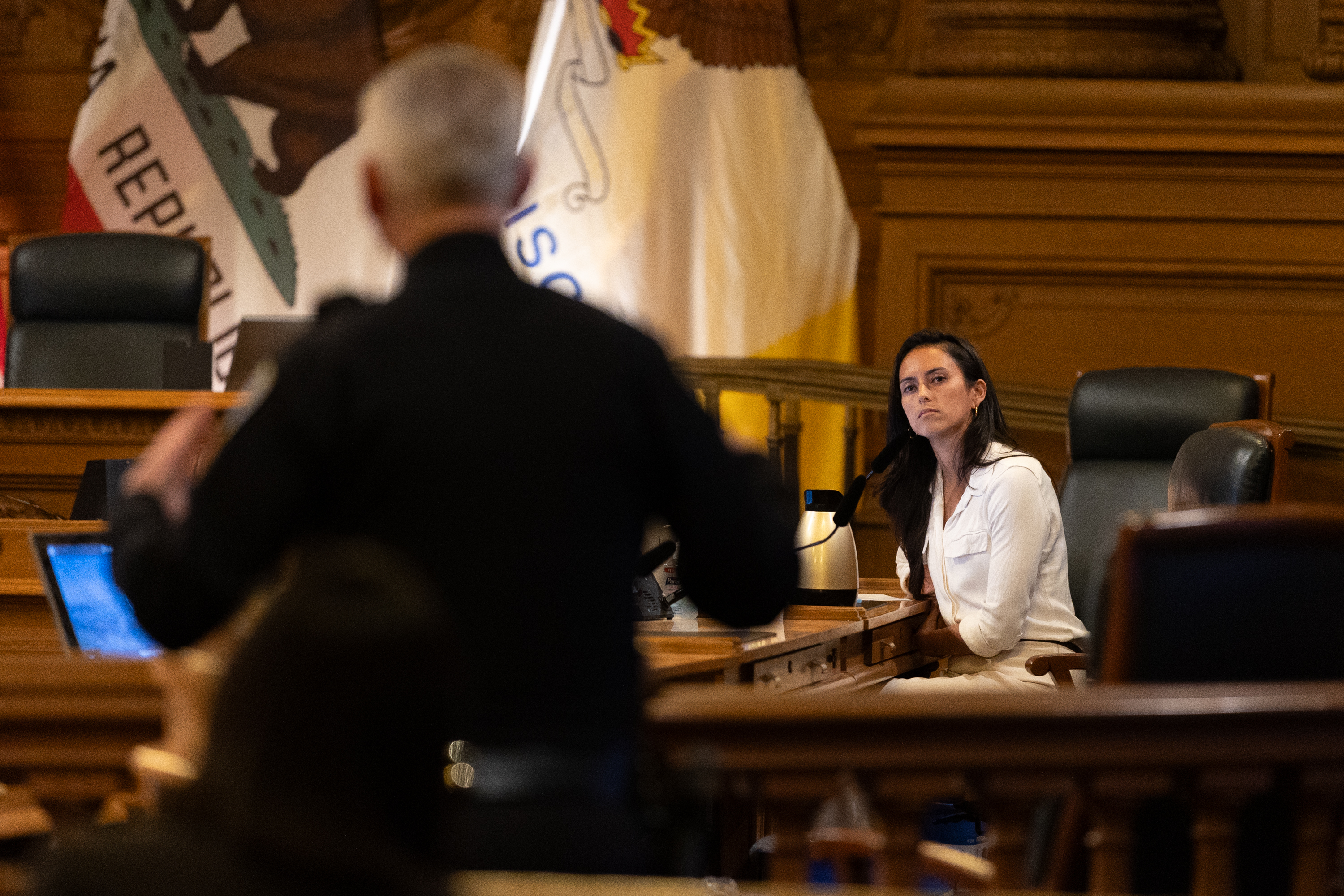 A woman seated in the background looks at an SFPD assistant chief in the foreground in a board room.