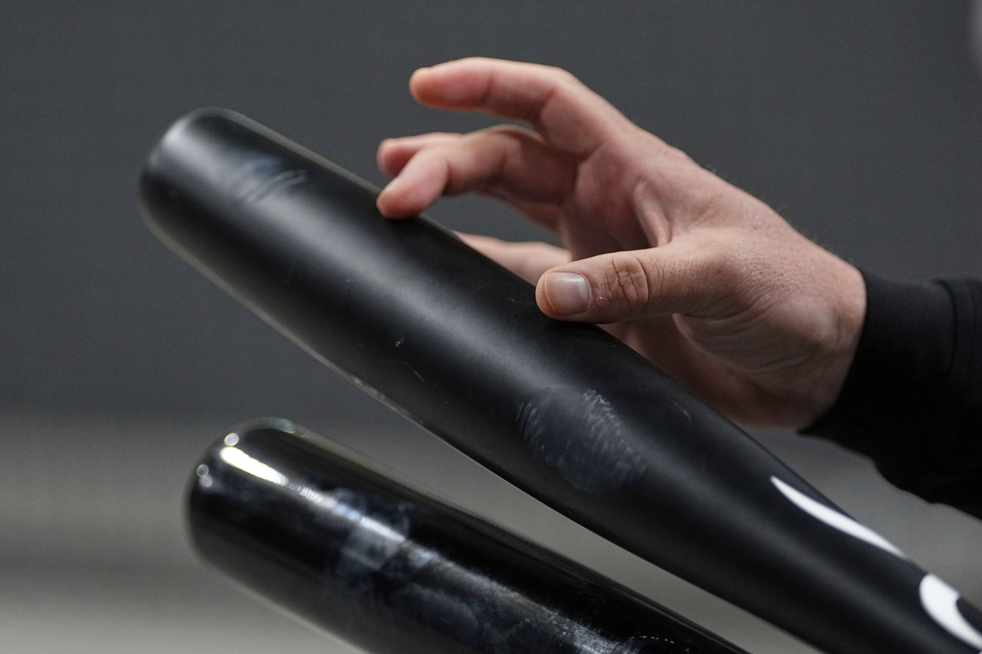 A person's hand is holding a black baseball bat horizontally. The bat appears slightly scuffed and worn, with a second bat partially visible below.