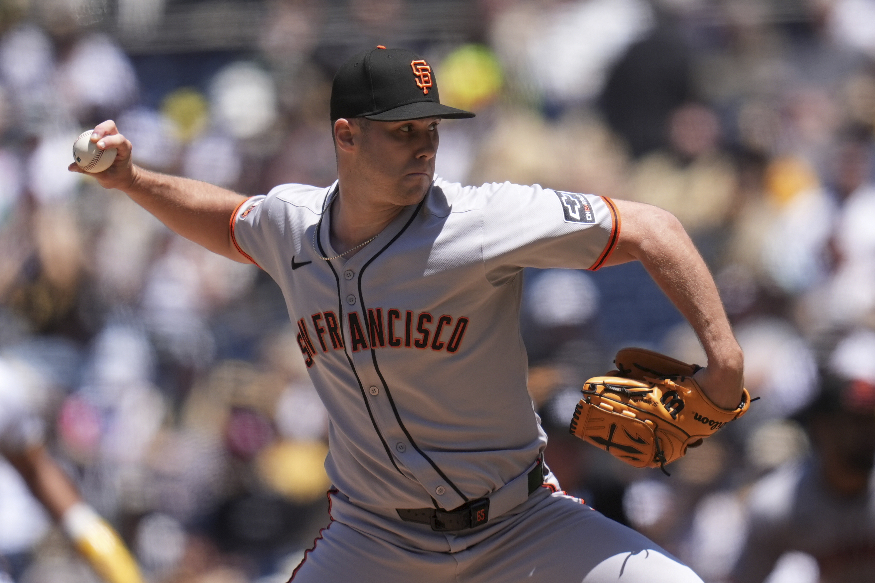 A baseball player wearing a gray &quot;San Francisco&quot; jersey pitches during a game. He holds a baseball in one hand and a glove in the other, focused on his throw.