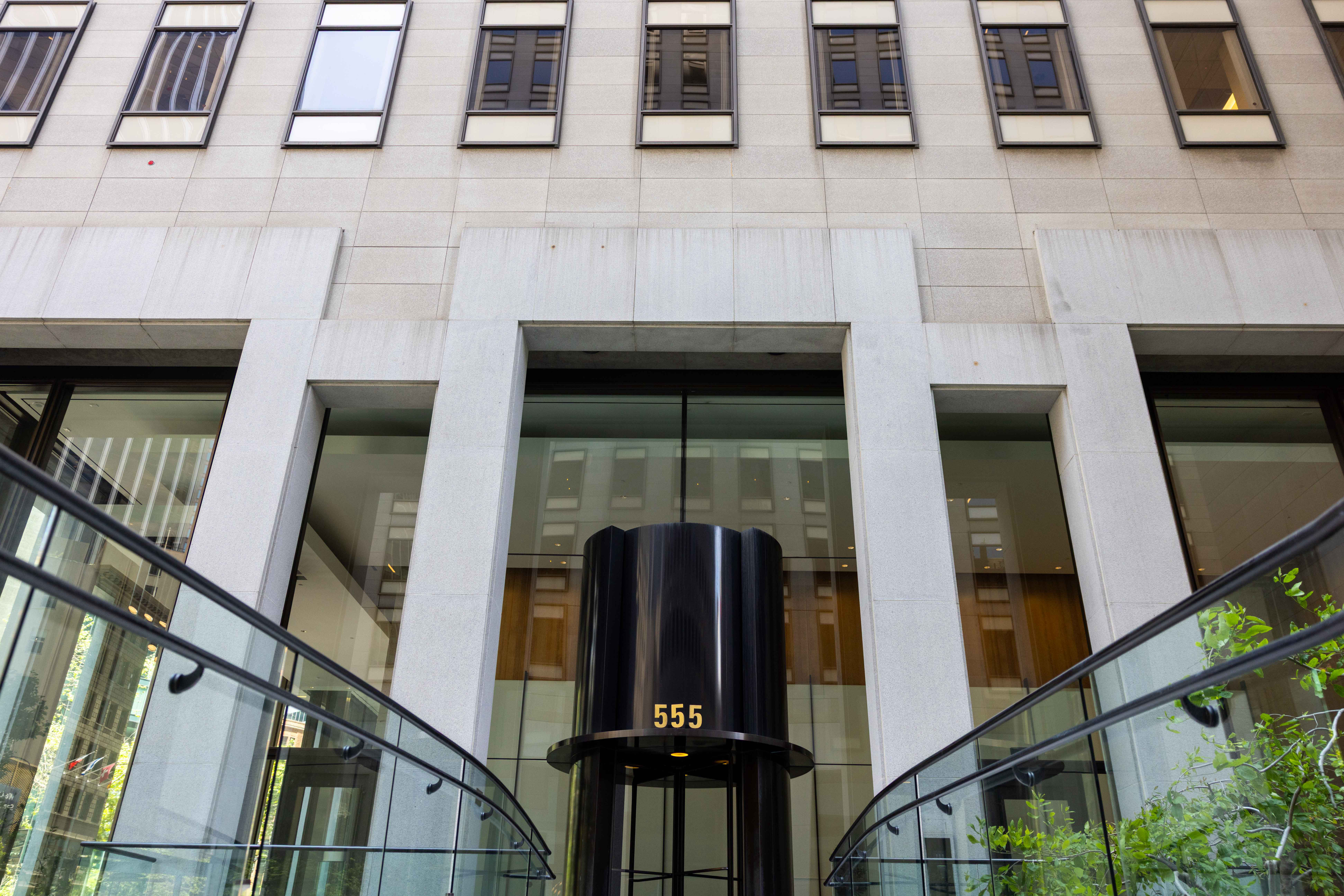 The image shows a modern building entrance with large windows and a black circular structure displaying the number 555, flanked by glass railings.