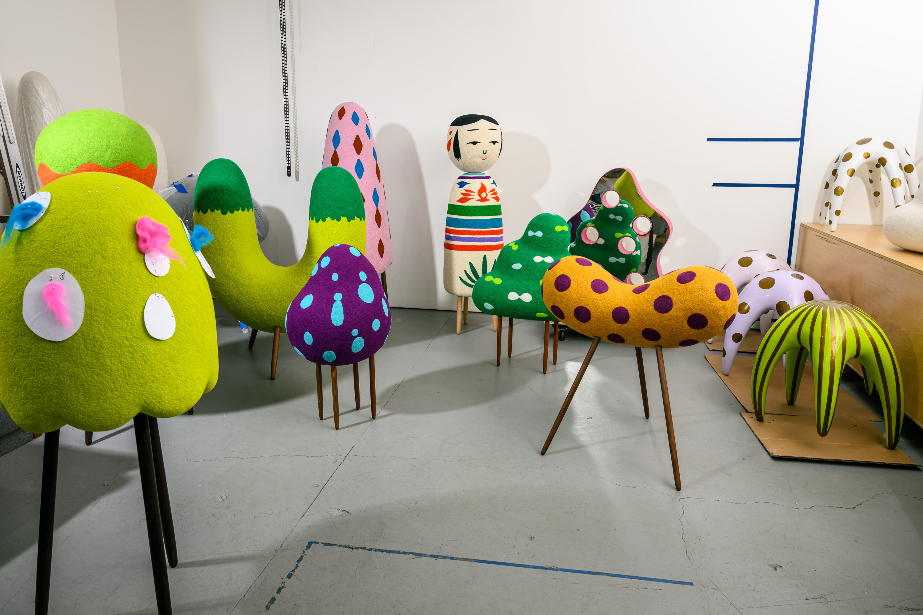 The image shows colorful, abstract sculptures resembling whimsical furniture with various patterns and shapes. There's also a mannequin-style figure with a painted face.