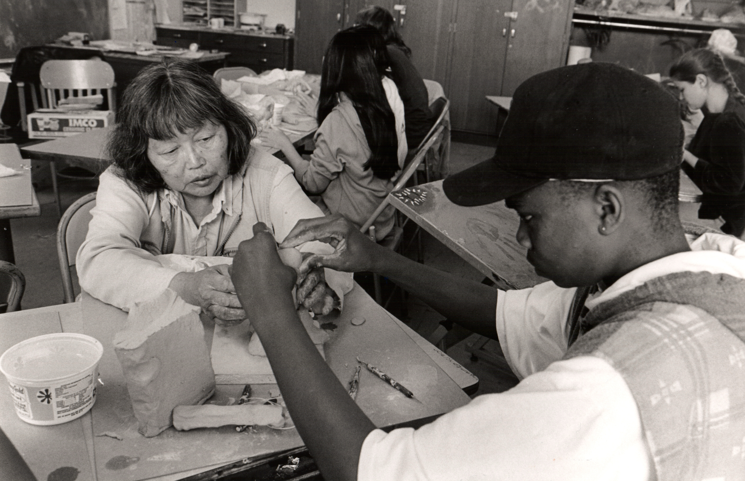 A teacher and a student are engaged in a hands-on clay sculpting activity. The teacher is guiding the student, who is focused on shaping the clay.