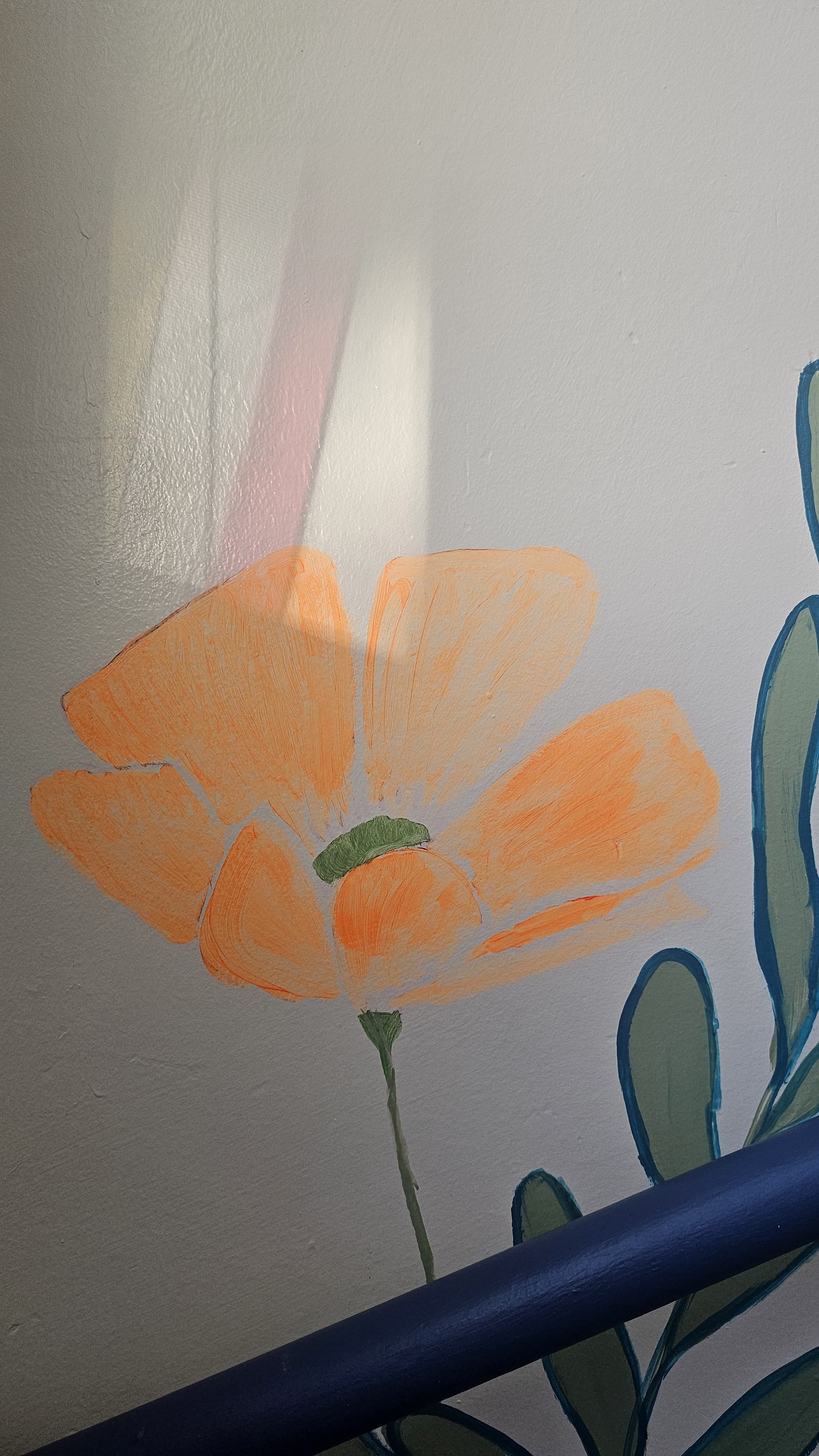 An orange flower with green leaves is painted on a wall. A diagonal shadow and a dark blue railing run across the lower part of the image.