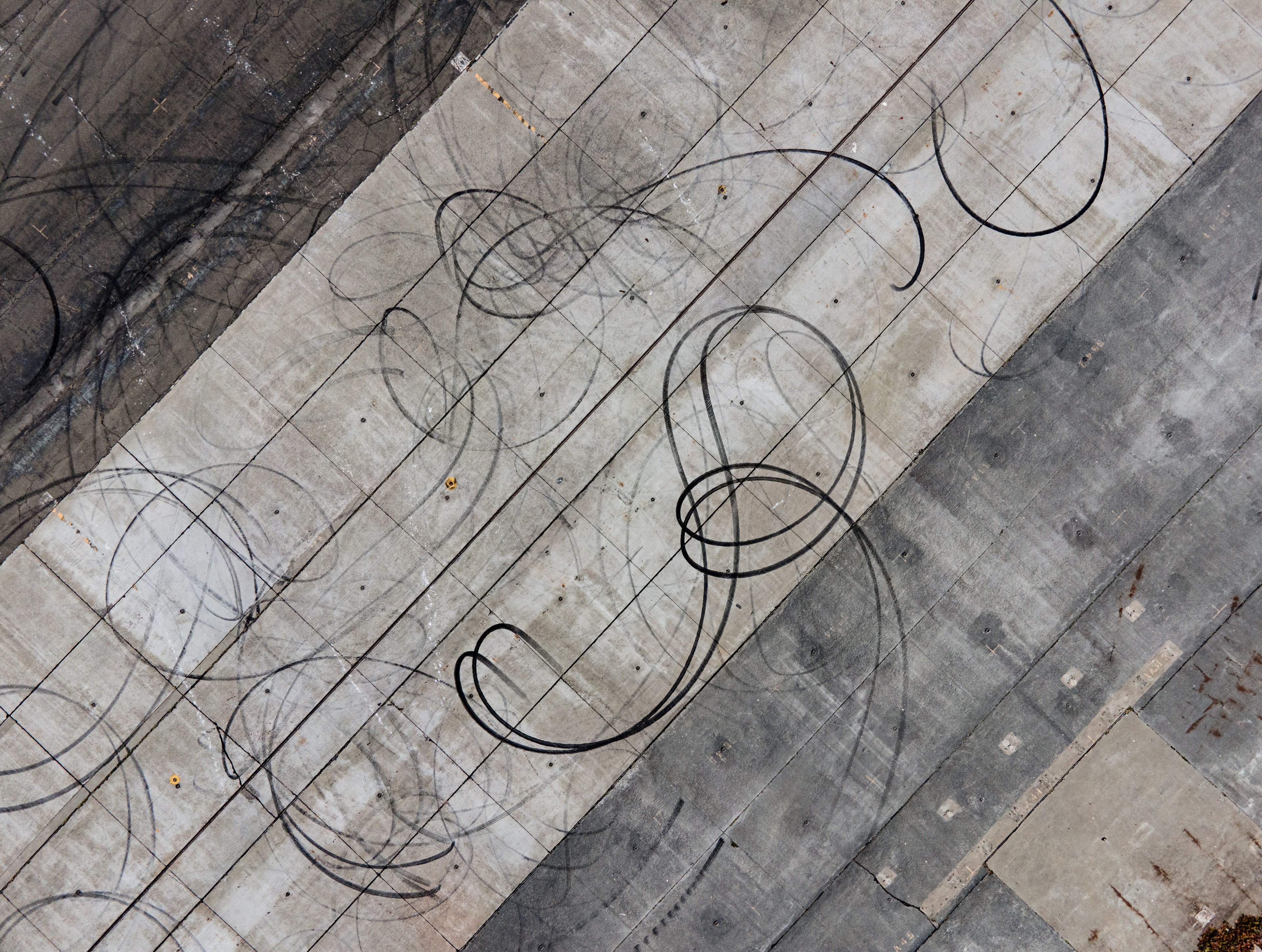 The image shows an aerial view of a concrete surface with looping tire skid marks on it, suggesting vehicle activity like drifting or spinning.from above. 
