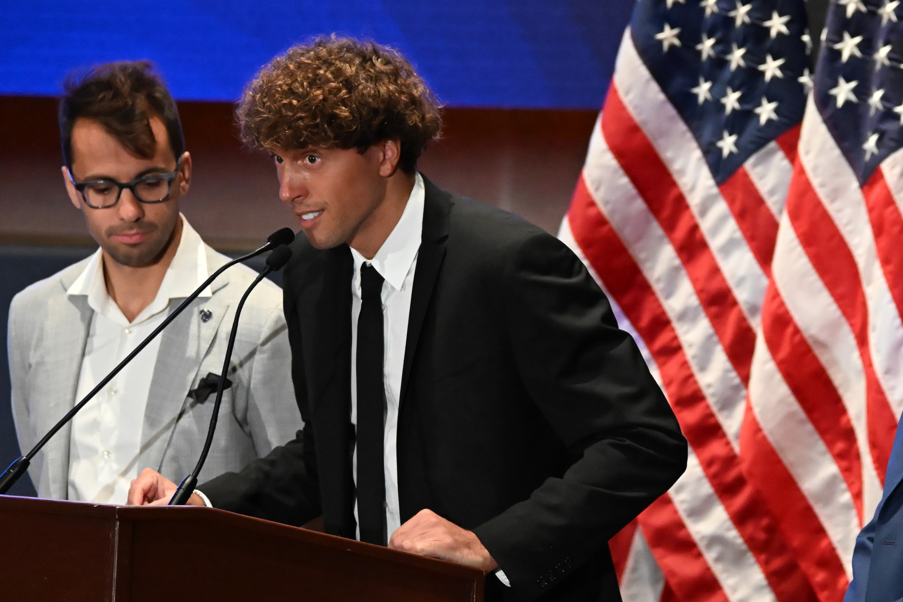 Man talking on podium in front of American flag.
