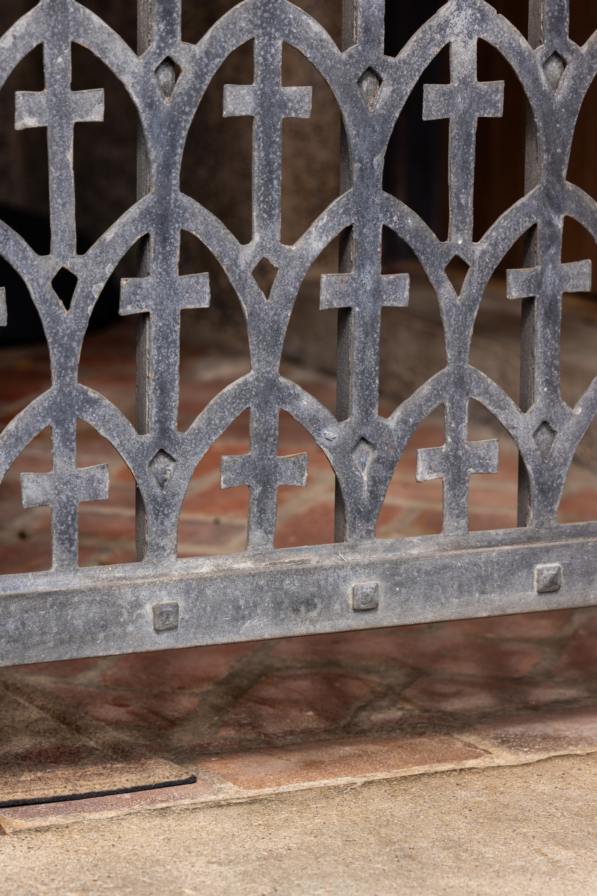 The image shows a decorative metal gate with an intricate pattern of crosses and arches. The gate is situated over a tile floor.