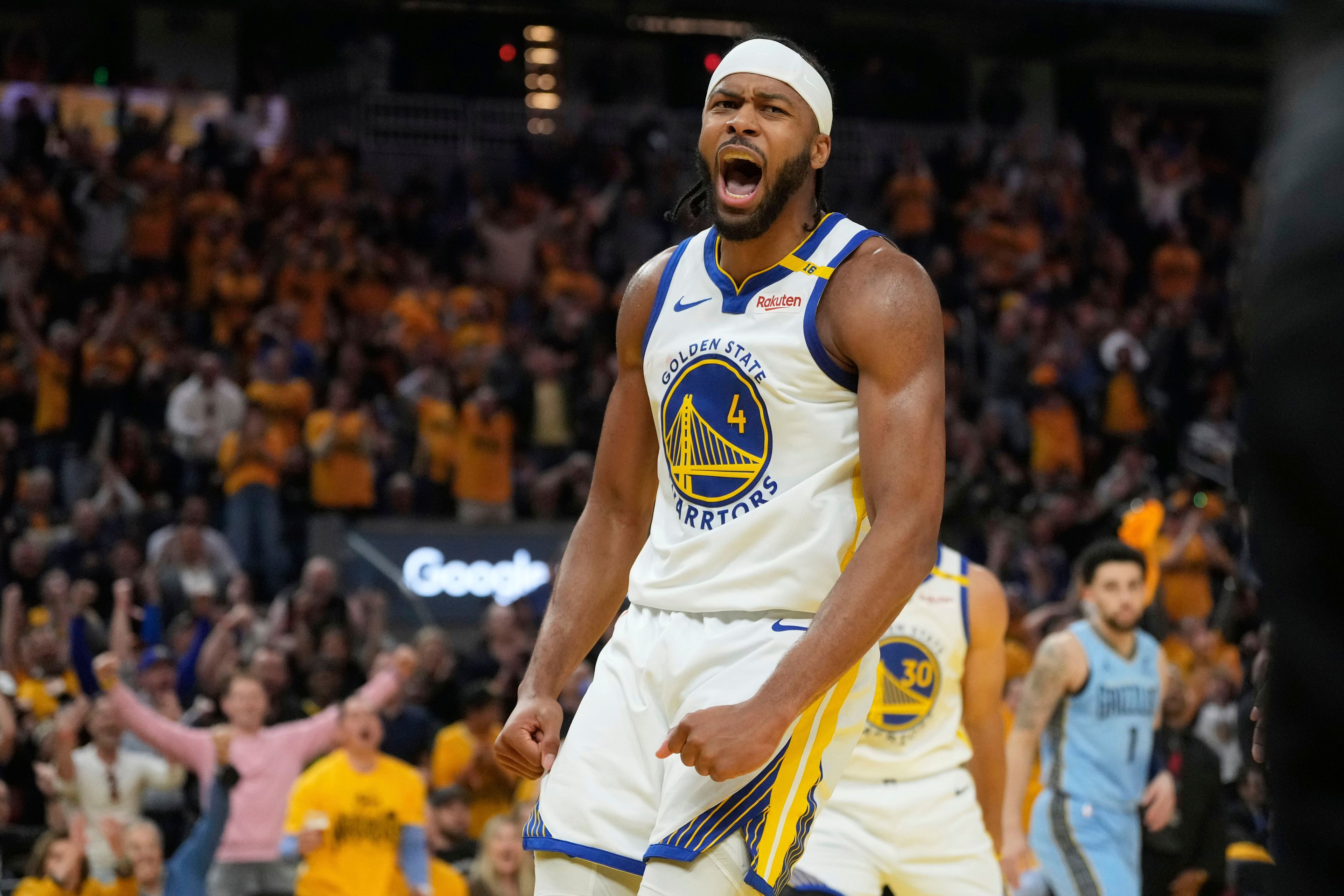 A basketball player in a Golden State Warriors jersey is passionately celebrating on the court, with an excited crowd in the background.