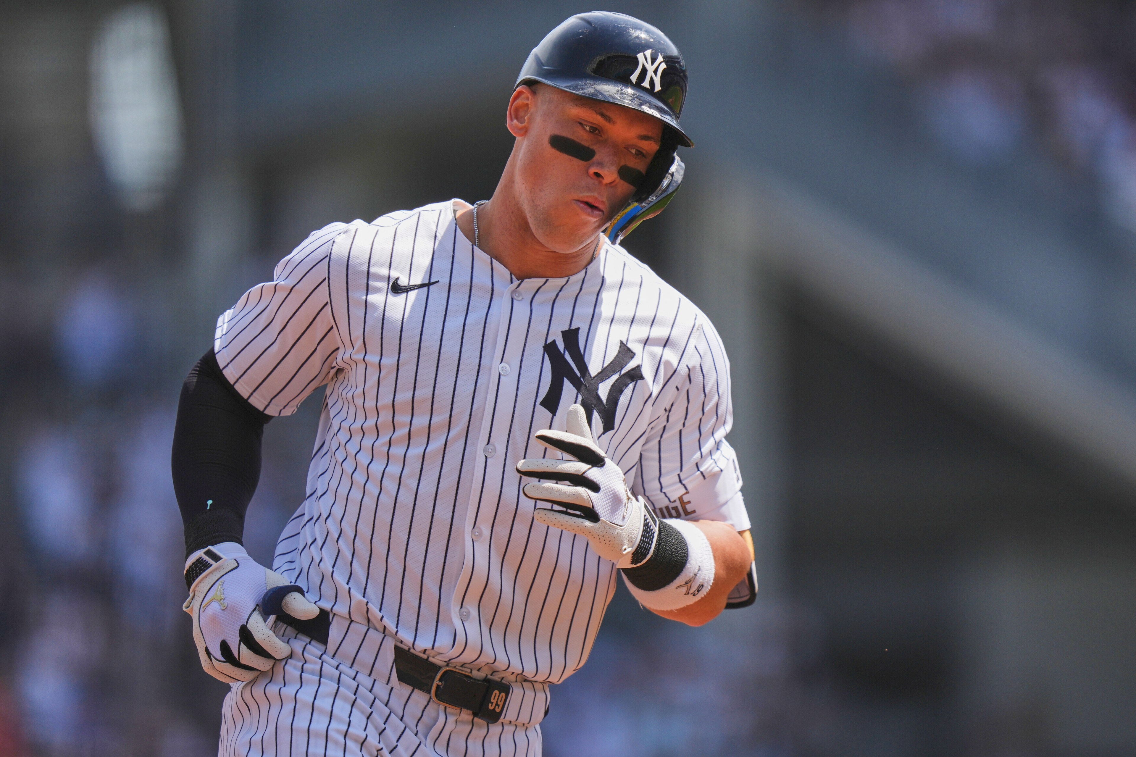 A baseball player, wearing a pinstriped uniform and black helmet, is running. He has black eye paint and is in motion with a blurred background.