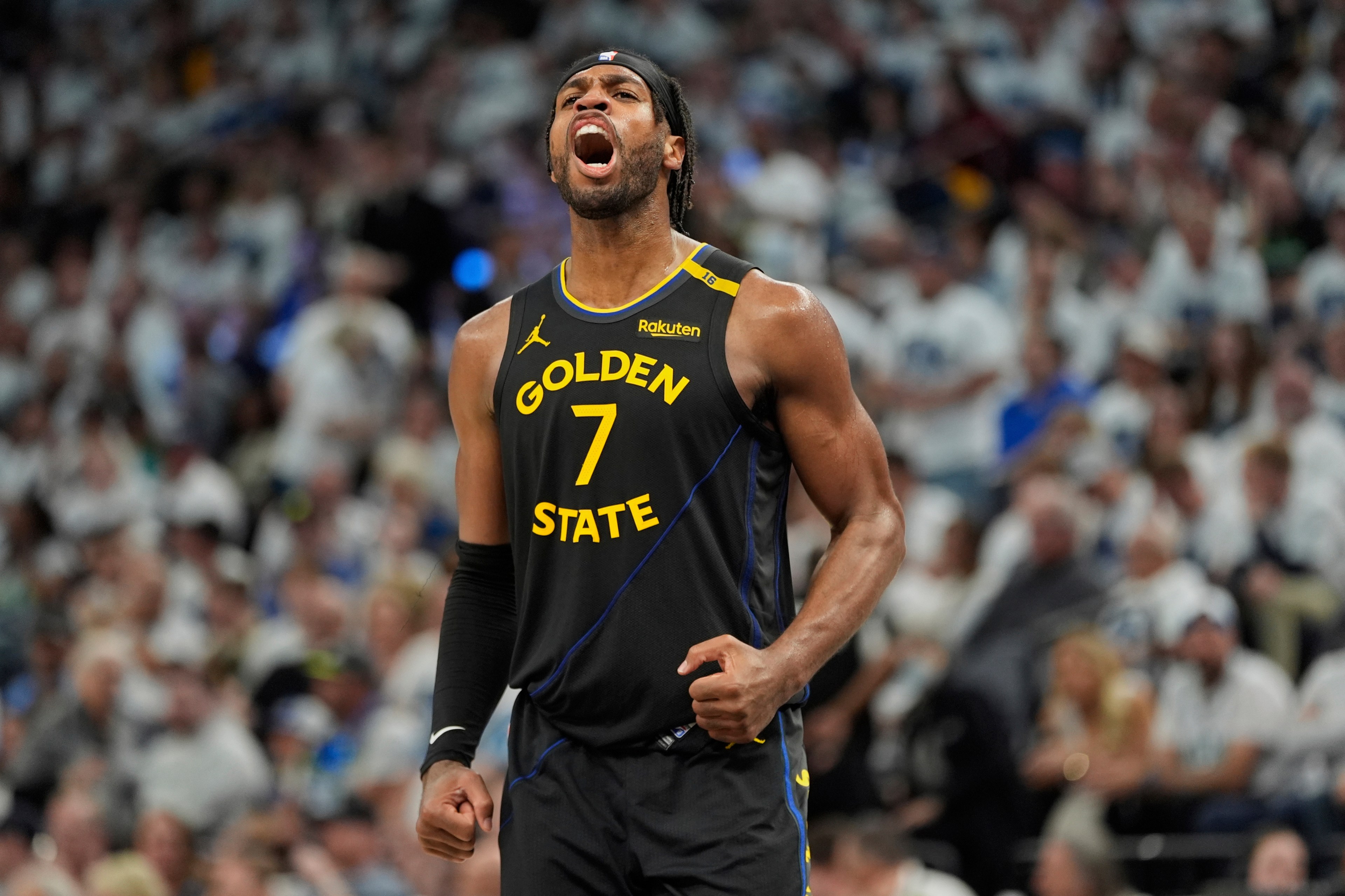 A basketball player in a black &quot;Golden State&quot; jersey, number 7, is passionately shouting on the court, with a crowd blurred in the background.