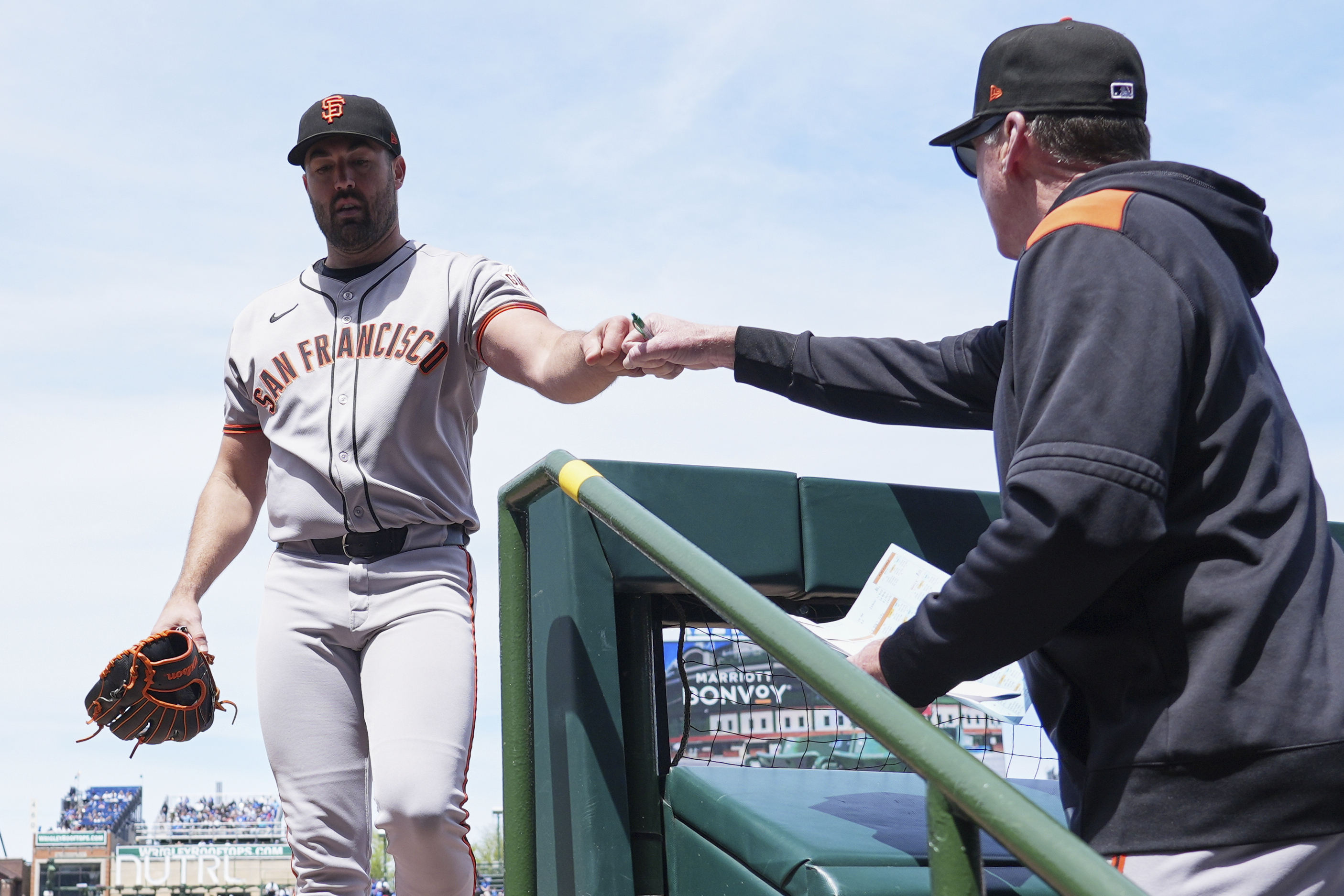 A baseball player in a San Francisco uniform, holding a glove, receives an item from another person in a team hoodie on a stadium staircase.