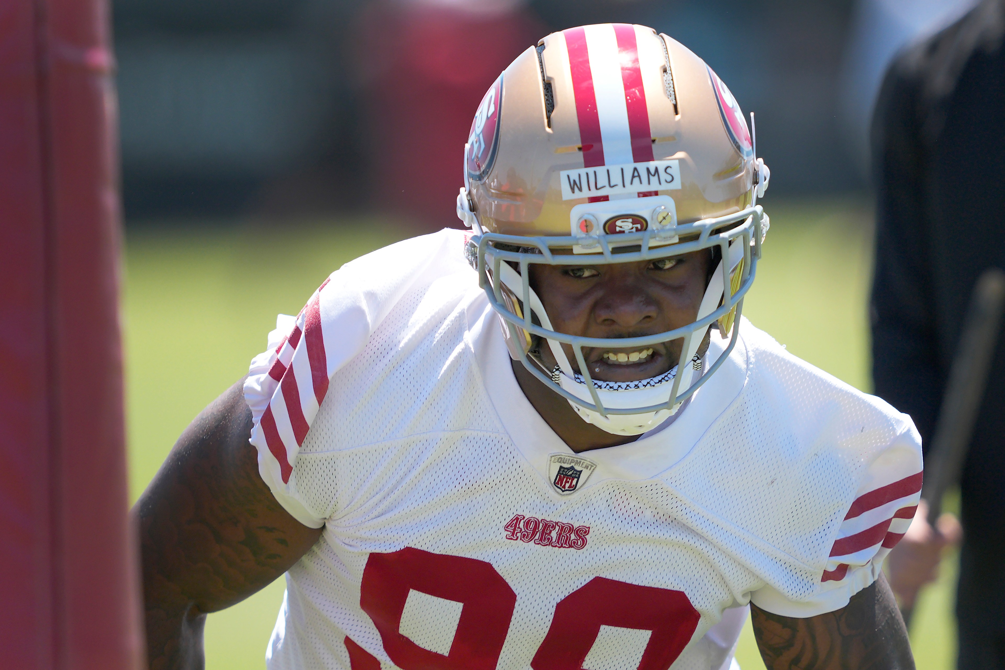 An athlete wearing a football helmet and white jersey with red stripes, marked "49ers" and number 90, is intensely focusing during training.