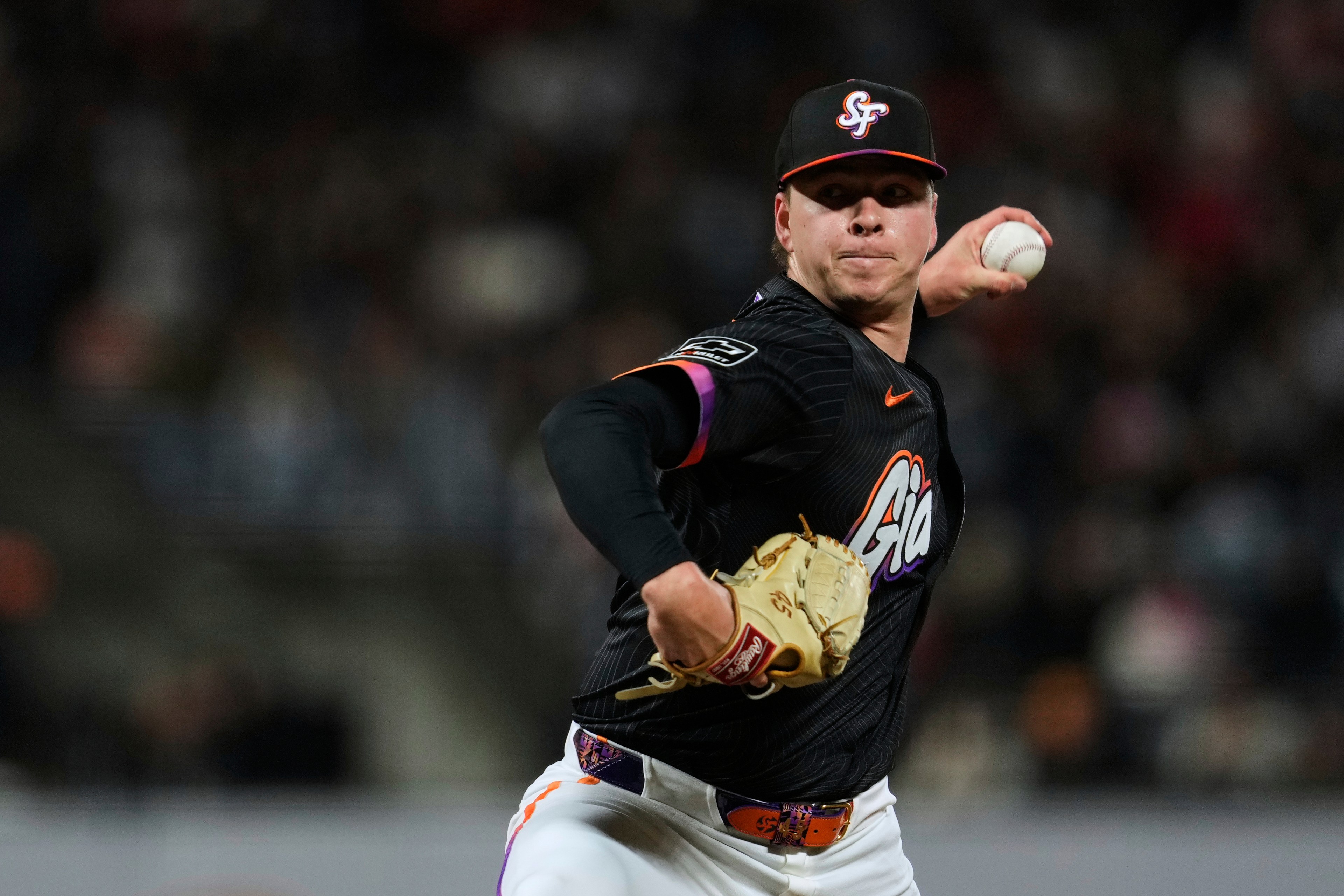 A baseball pitcher in a black uniform is mid-throw on the mound, wearing a cap with &quot;SF&quot; and holding a ball in his right hand and a glove on the left.