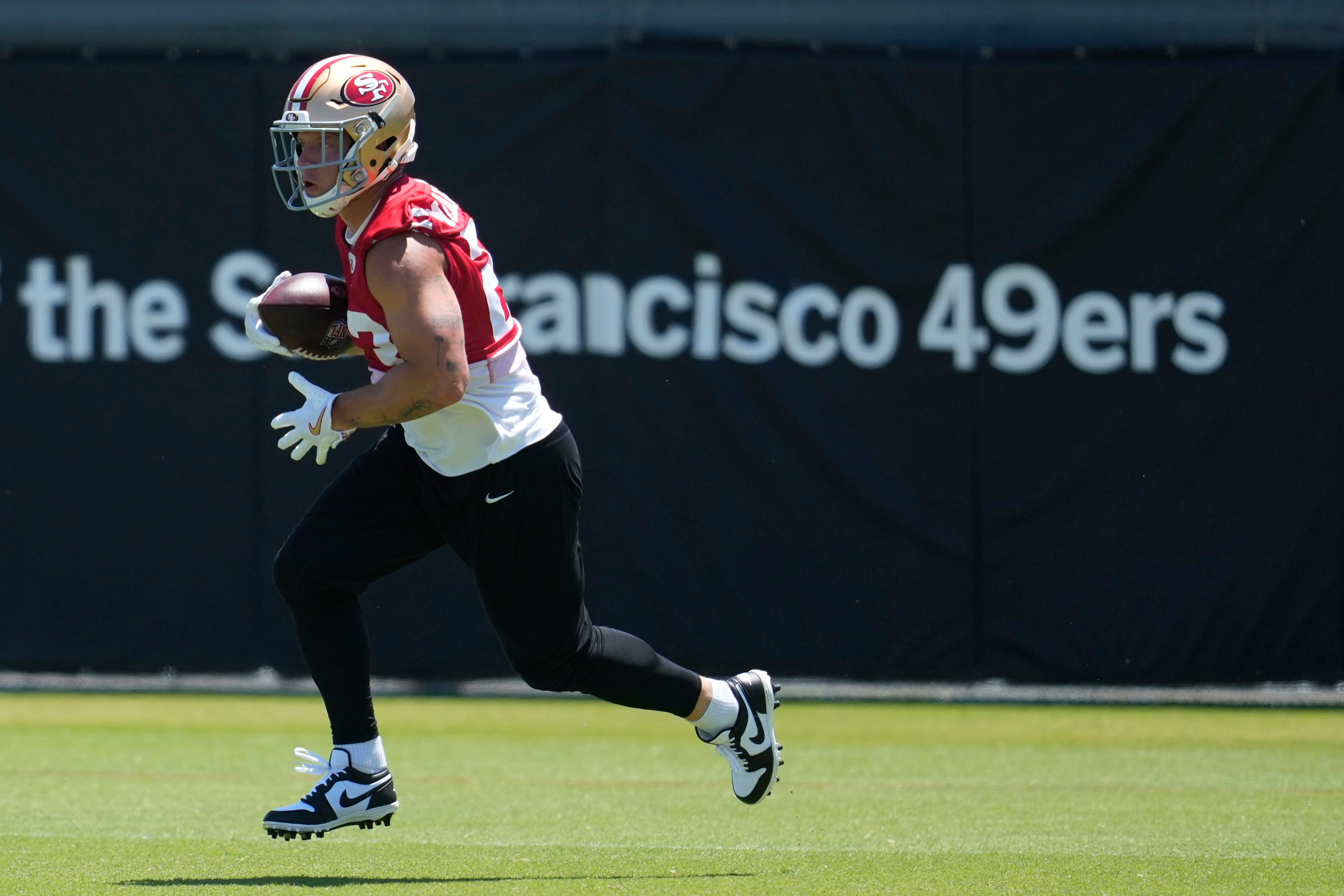 A football player in a 49ers jersey runs on a field, holding a football. A black background displays "San Francisco 49ers" in white text.