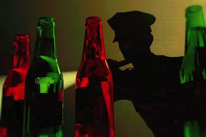 A police officer shining a light at beer bottles.