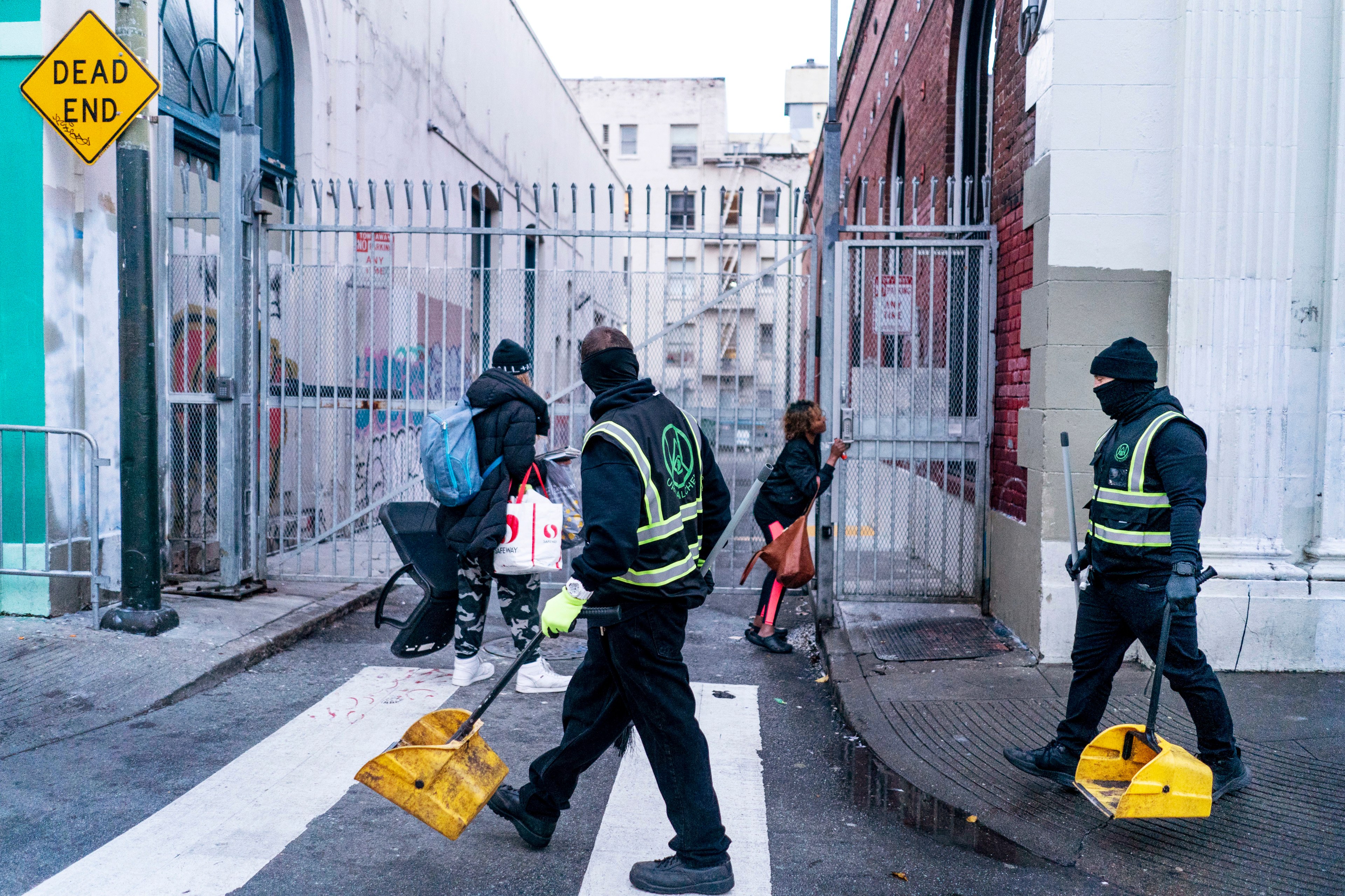 Uniformed Urban Alchemy staff carry dustbins walking through the Tenderloin.