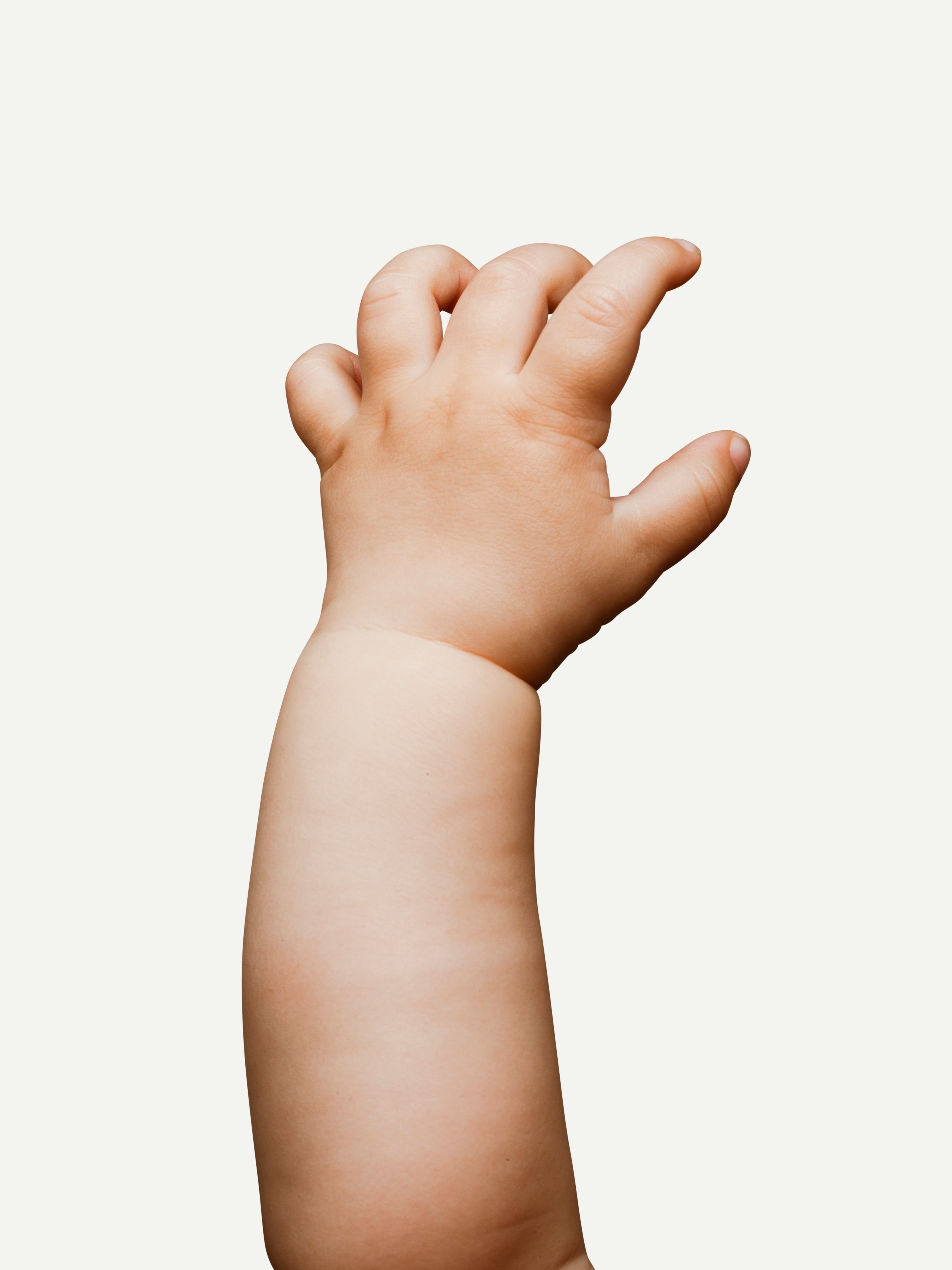 A baby's chubby arm is reaching upward against a plain white background, with its fingers spread gently apart.