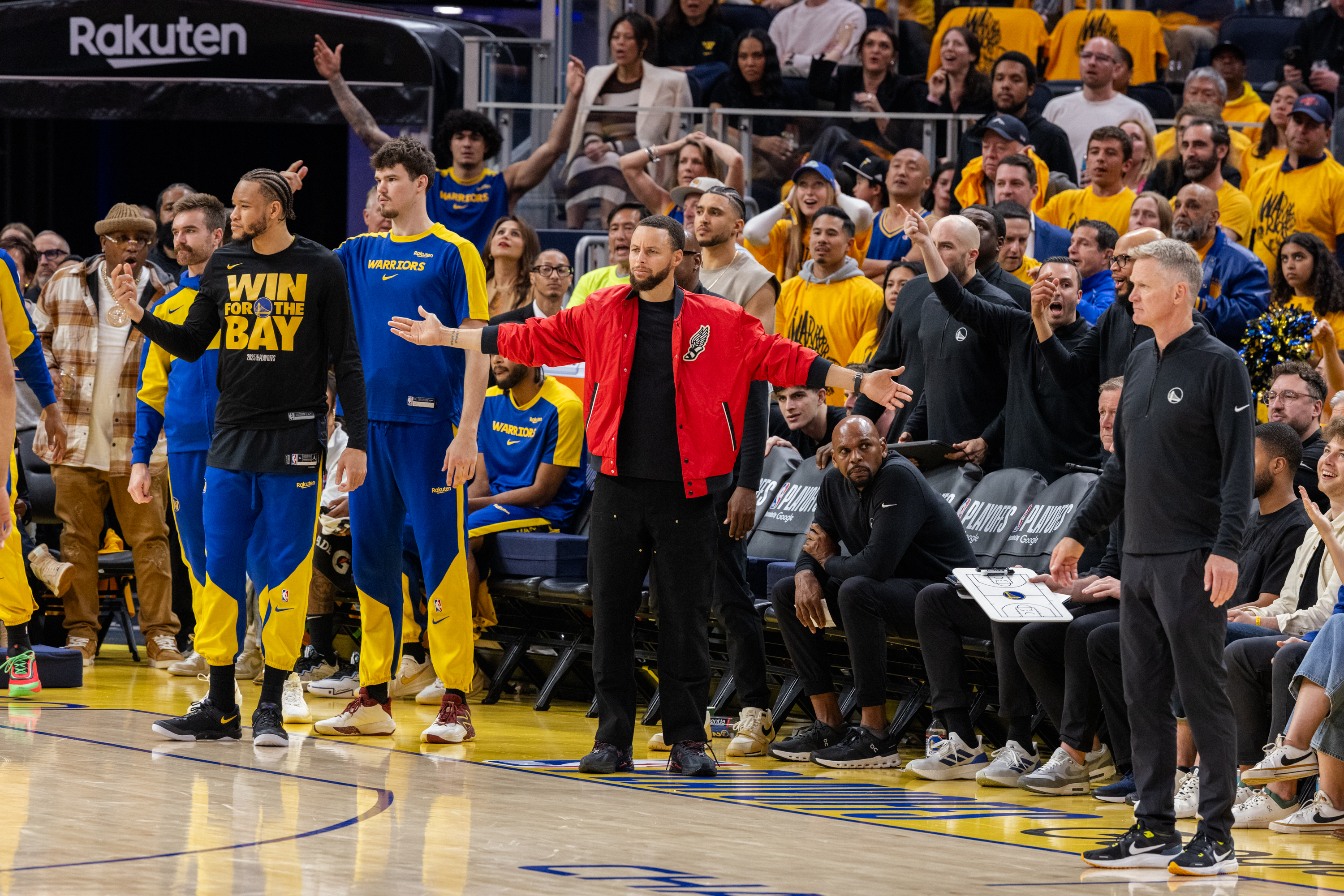 A group of people in sports attire stands on a basketball court. One person in a red jacket gestures passionately, while others in yellow and blue outfits look on.
