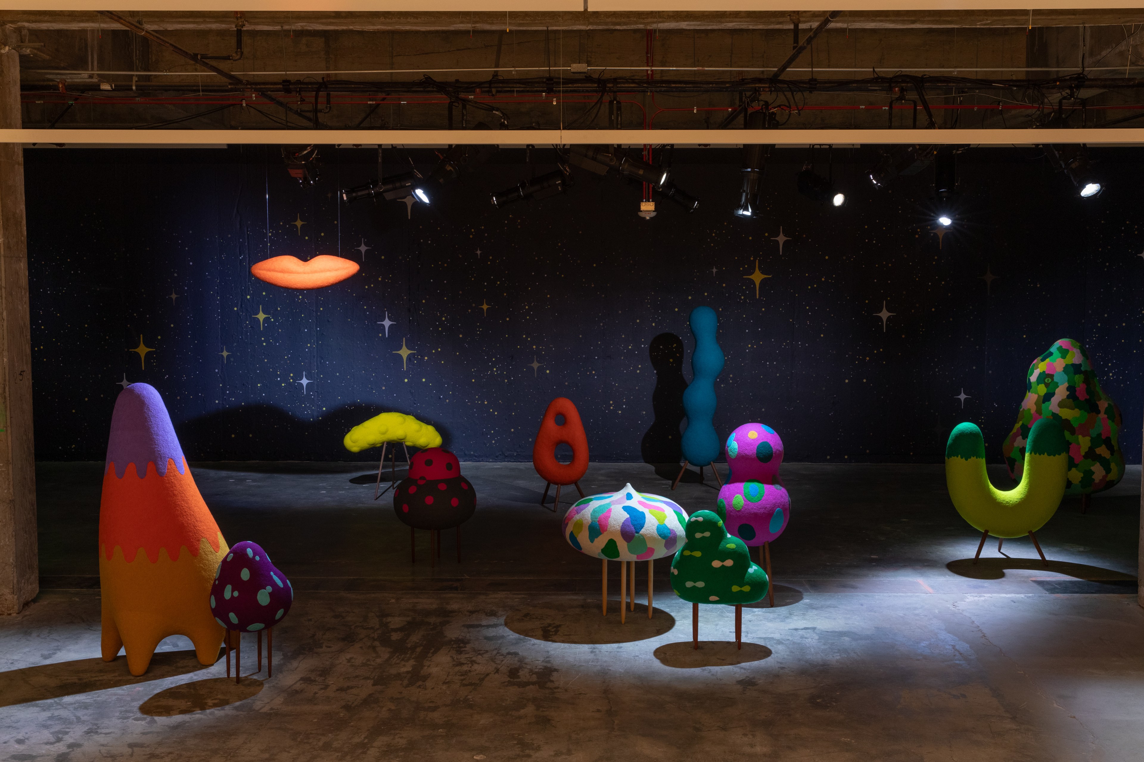 The image shows a room with colorful, abstract sculptures resembling mushrooms and clouds, set against a starry night sky backdrop.