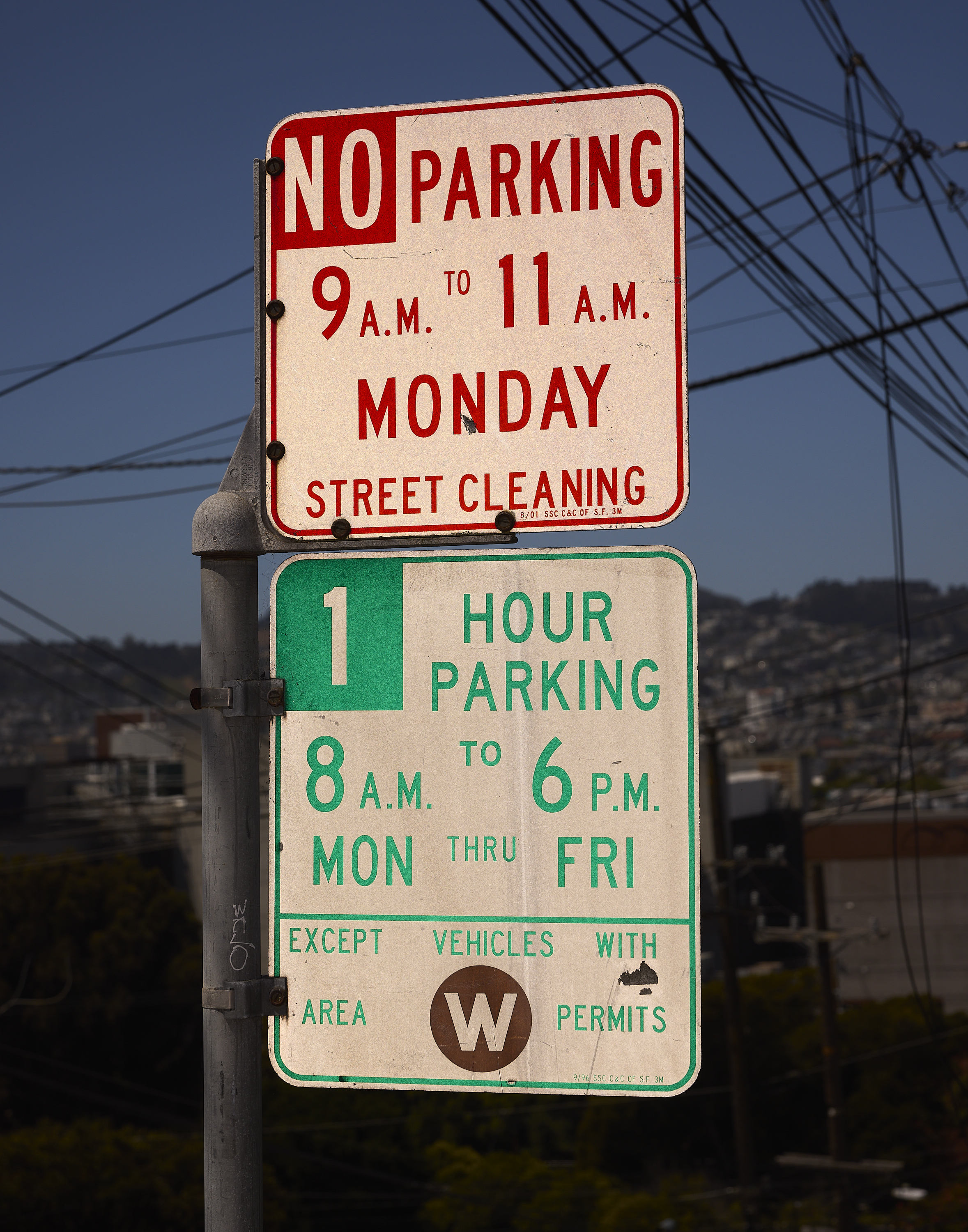 The image shows two parking signs on a pole. The top sign prohibits parking from 9-11 AM on Mondays for street cleaning. The bottom allows 1-hour parking 8 AM-6 PM, Mon-Fri, except for vehicles with area W permits.