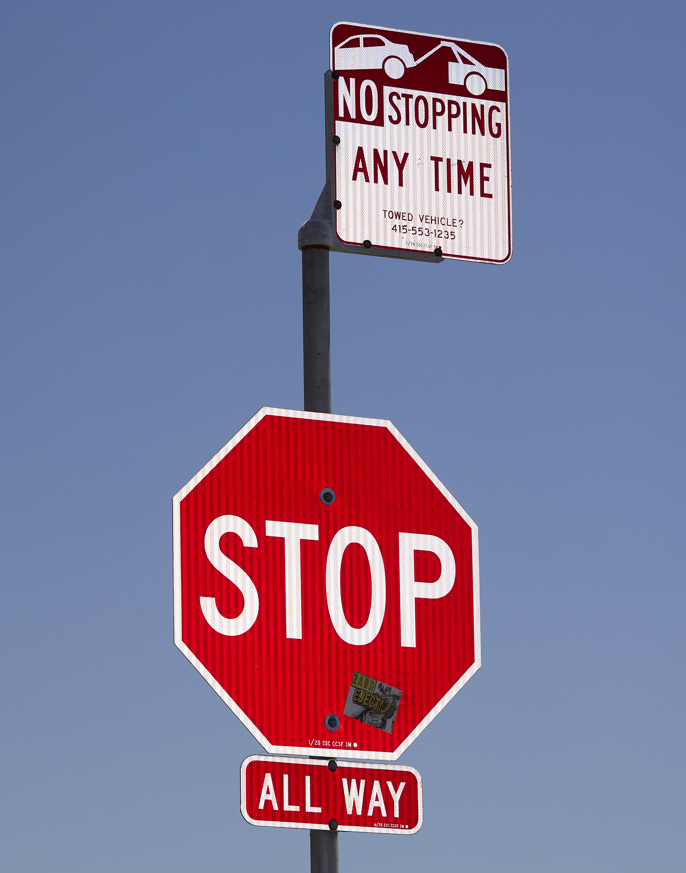 A &quot;STOP&quot; sign with an &quot;ALL WAY&quot; plaque is below a &quot;NO STOPPING ANY TIME&quot; sign on a pole, against a clear blue sky.