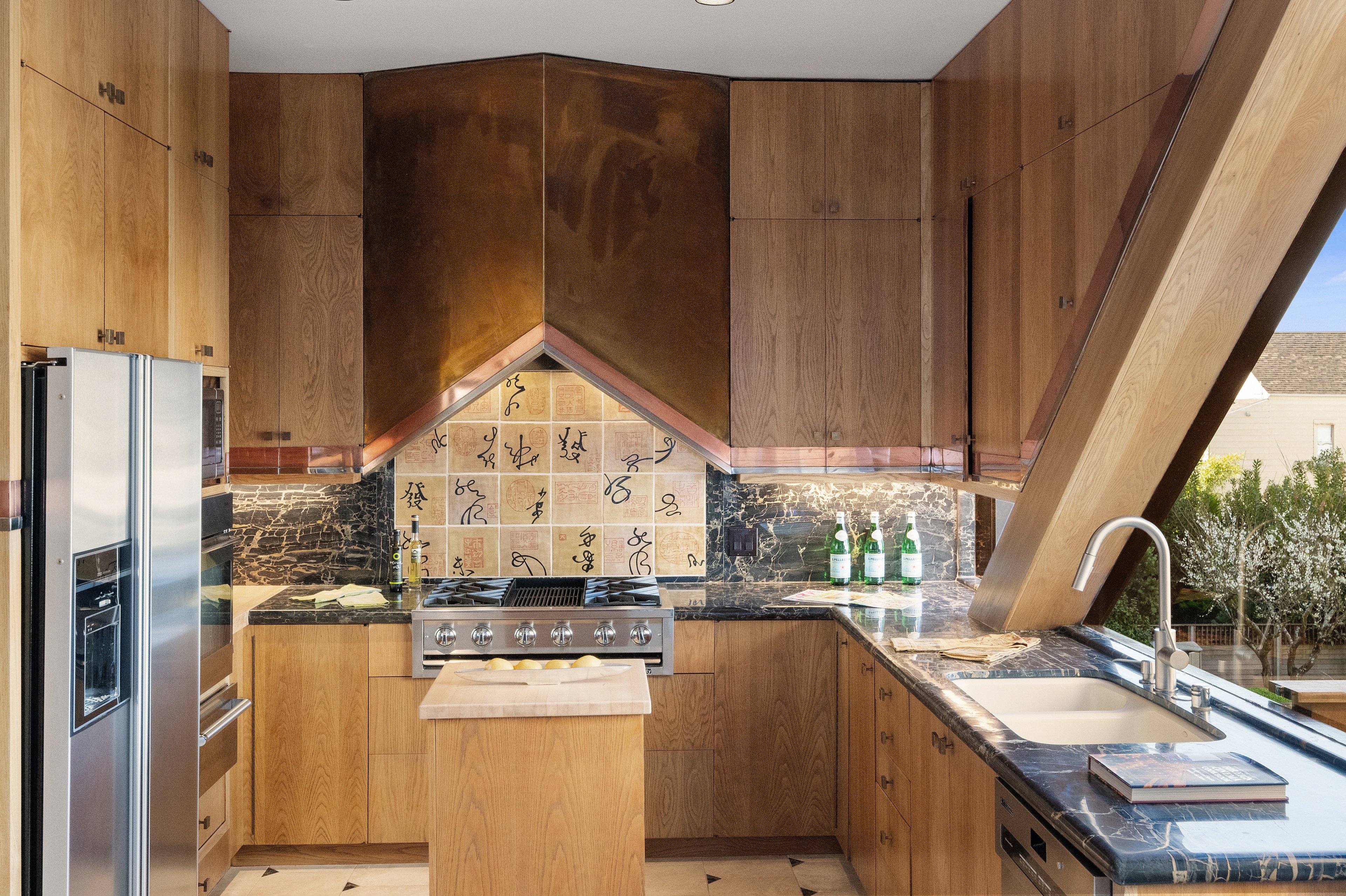 The kitchen features wood cabinets, a stainless steel fridge, a stove with unique tile backsplash, a marble countertop, and a sleek faucet.