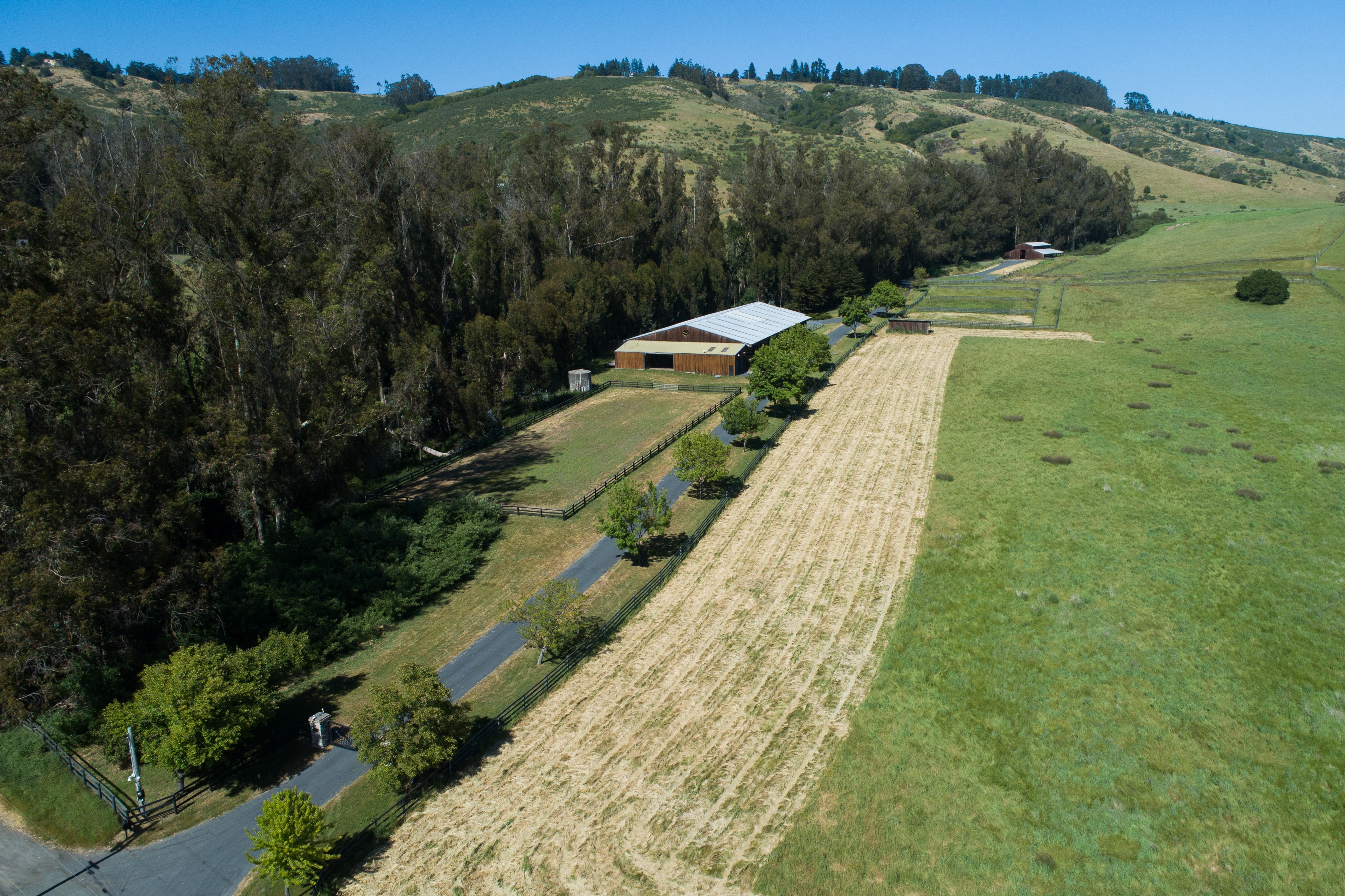 The image shows a rural landscape with a large barn, surrounded by fields and trees. A driveway runs alongside the barn, with hills in the background.
