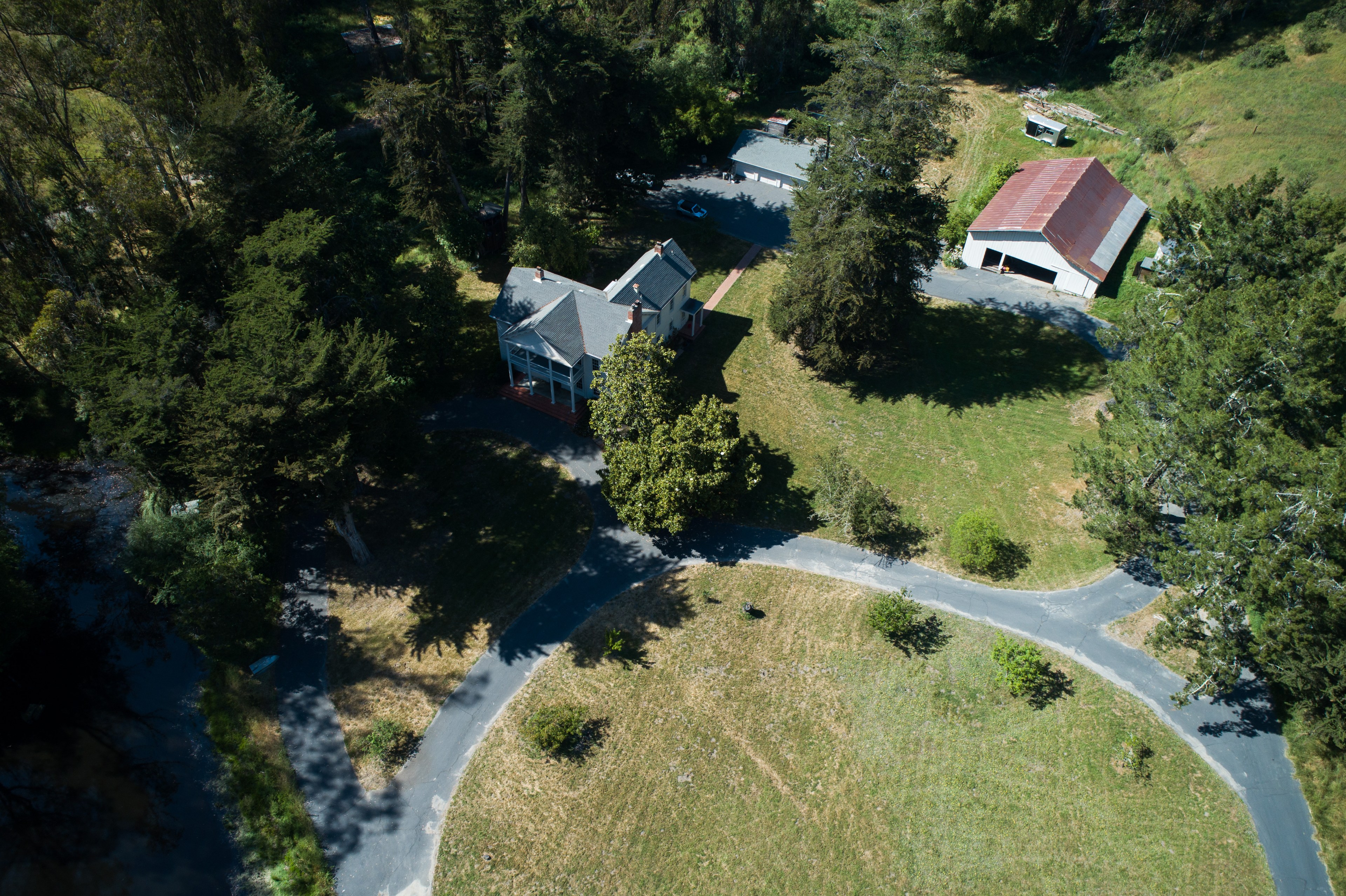 The image shows an aerial view of a large house with a gray roof, surrounded by trees. There's a driveway and a separate barn-like structure nearby.