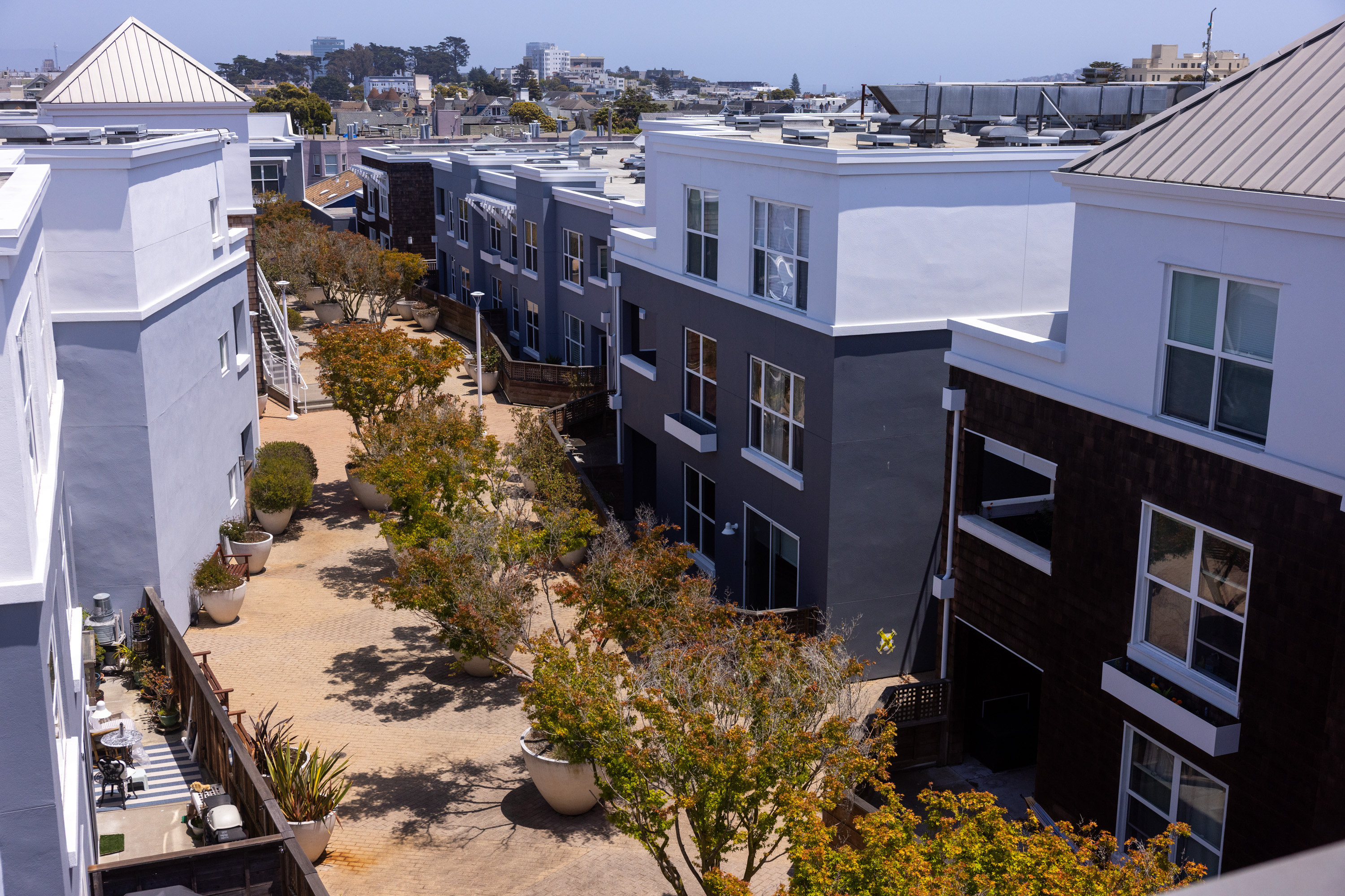 Aerial view of a modern apartment complex with multiple buildings in various shades of gray and white, featuring a tree-lined central pathway.