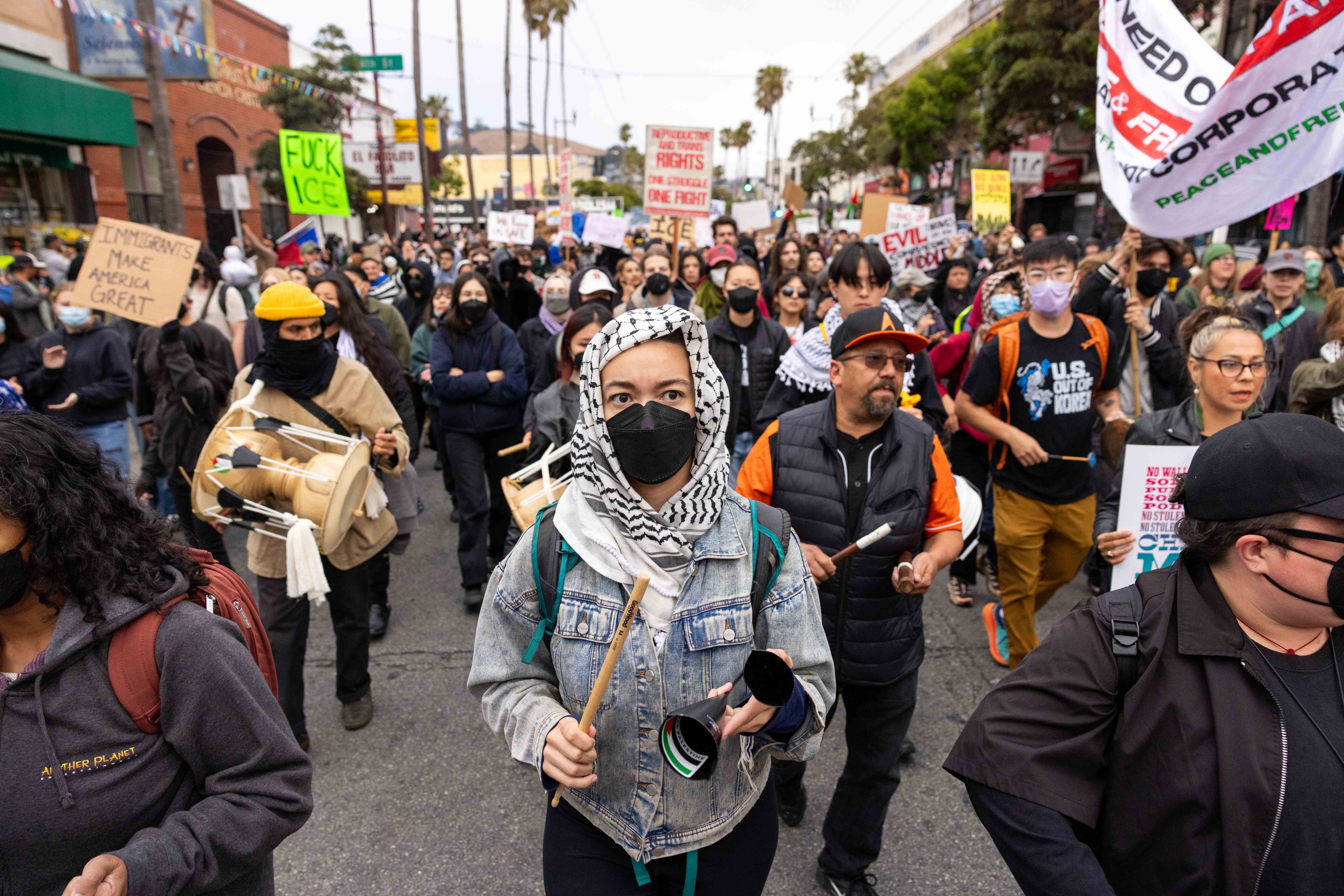 A large group of people are marching down a street, holding signs with messages like &quot;Immigrants Make America Great.&quot; Most are wearing masks.
