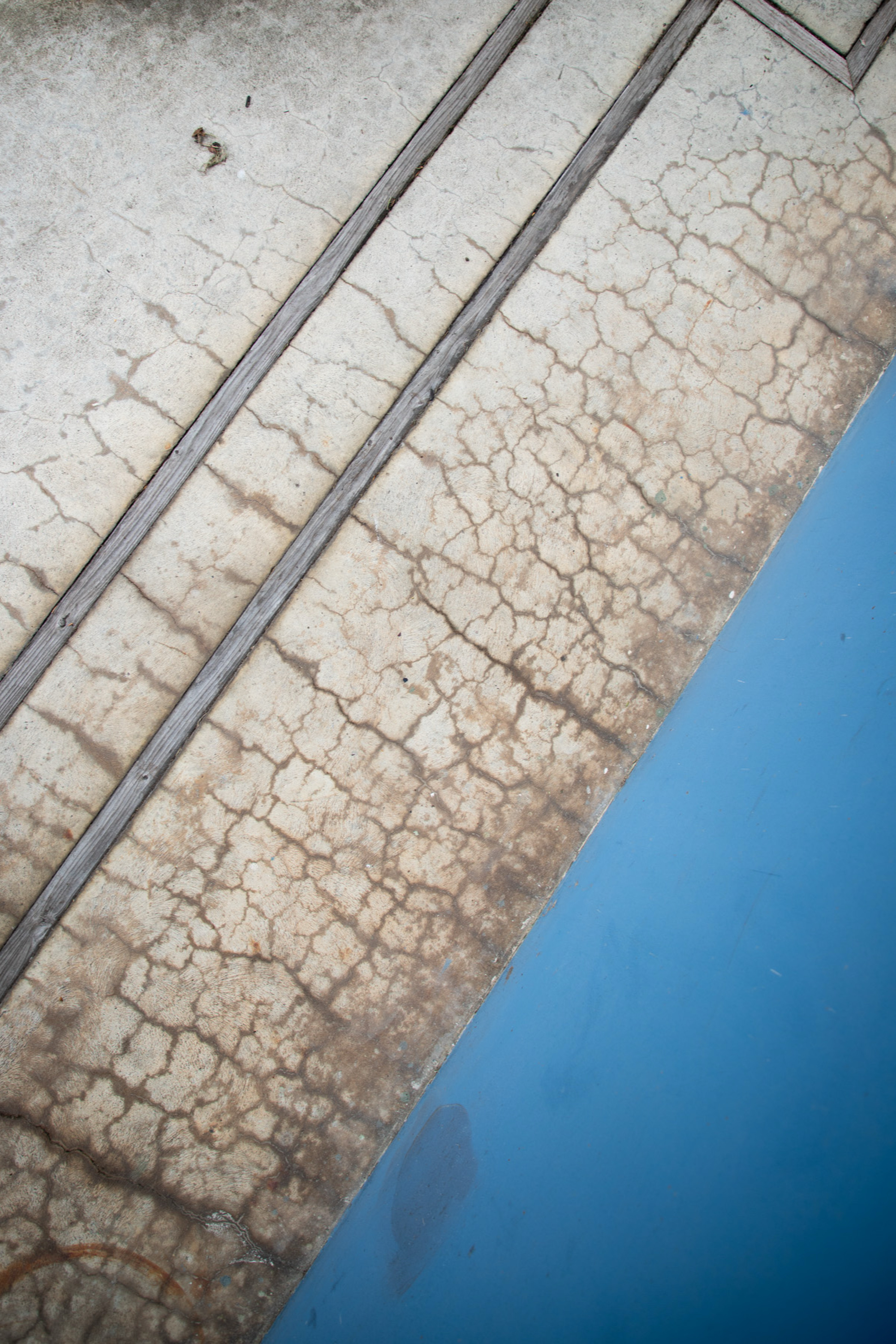 A cracked, weathered concrete surface with two parallel grooves is adjacent to a solid blue area, creating a striking contrast of textures and colors.