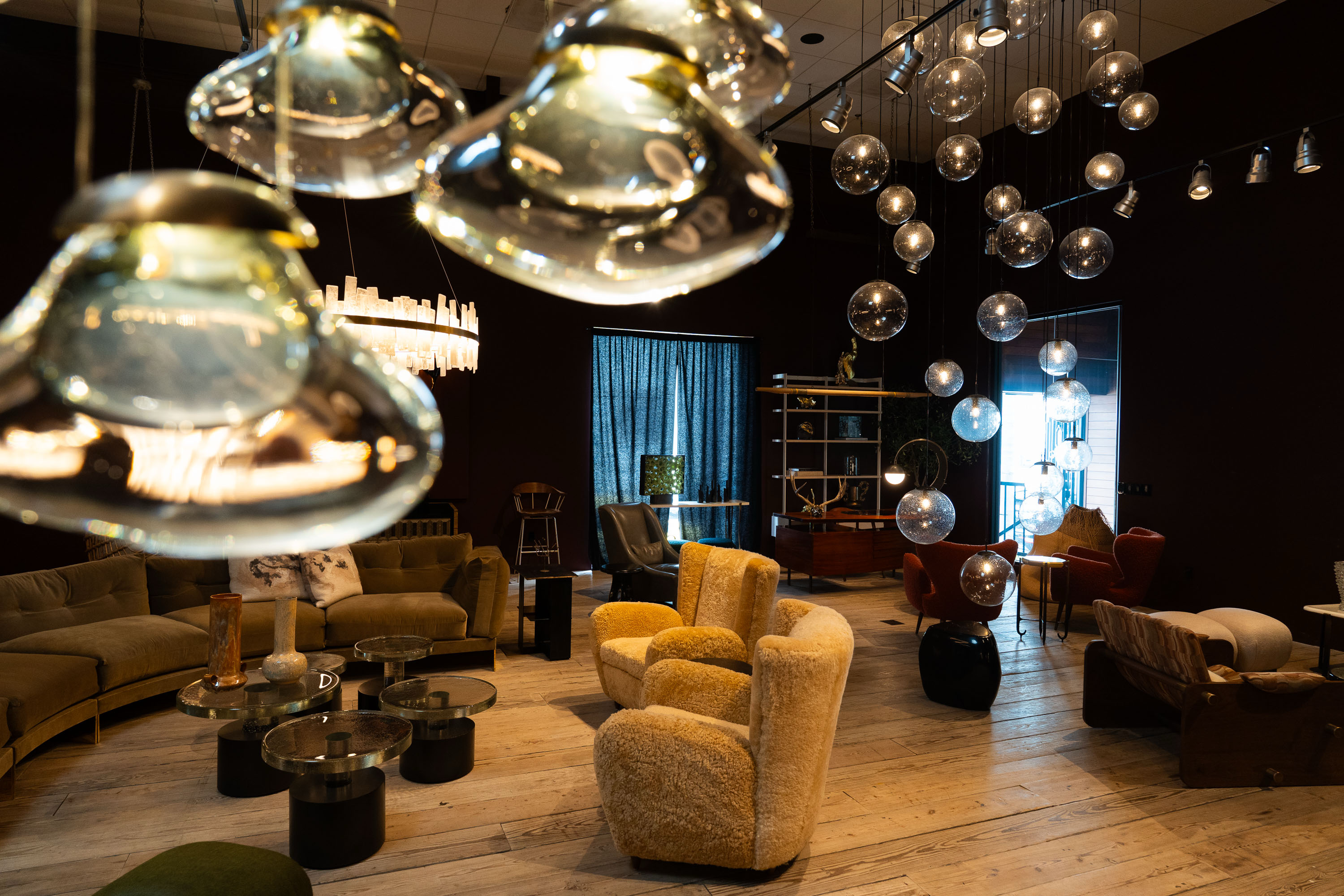 The image shows a stylish lounge with plush seating, glass bubble chandeliers, and a contemporary design. The room exudes a warm, inviting ambiance.