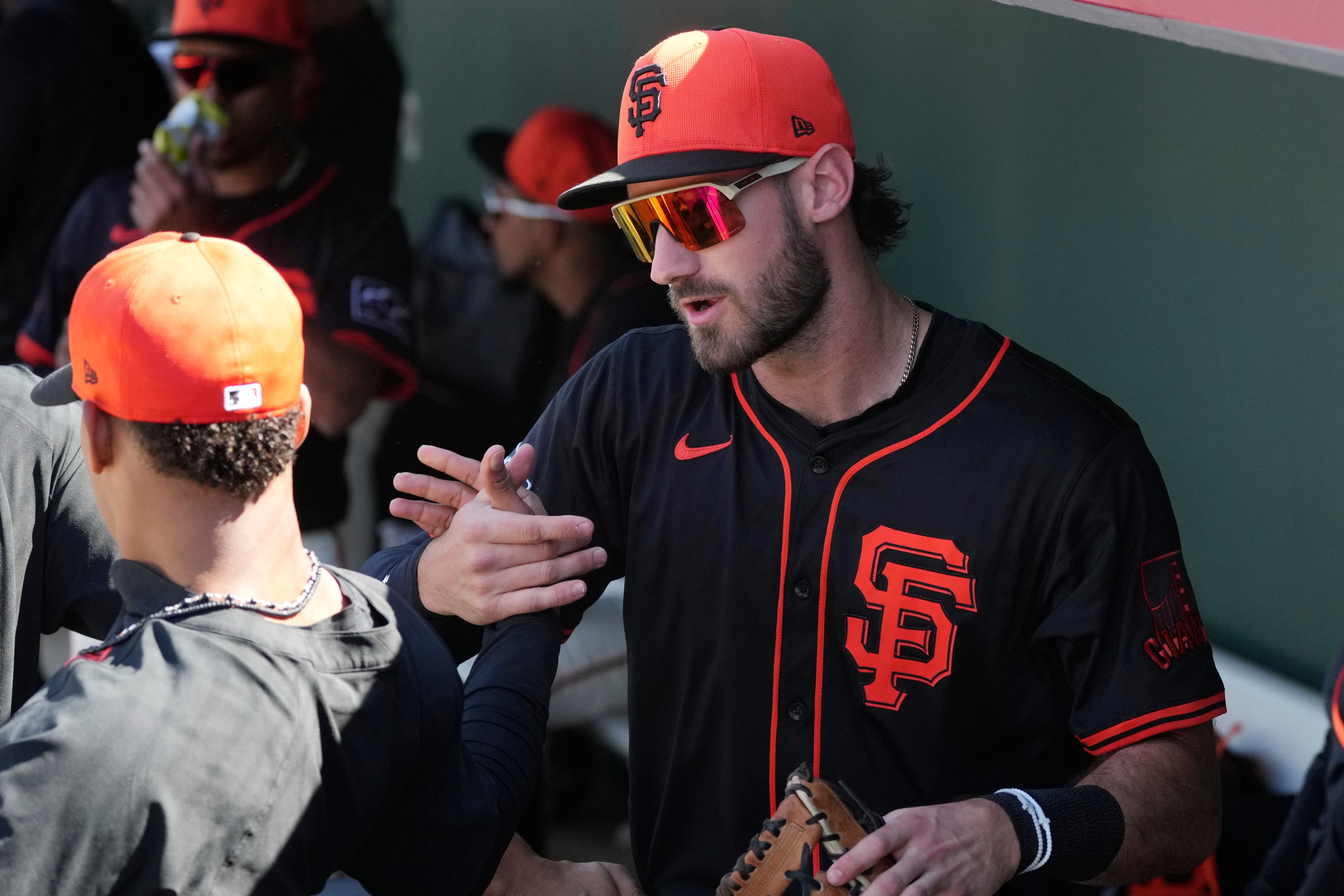 A baseball player wearing a black and orange uniform and cap with &quot;SF&quot; on it is giving a handshake in the dugout. He's holding a glove and wearing sunglasses.