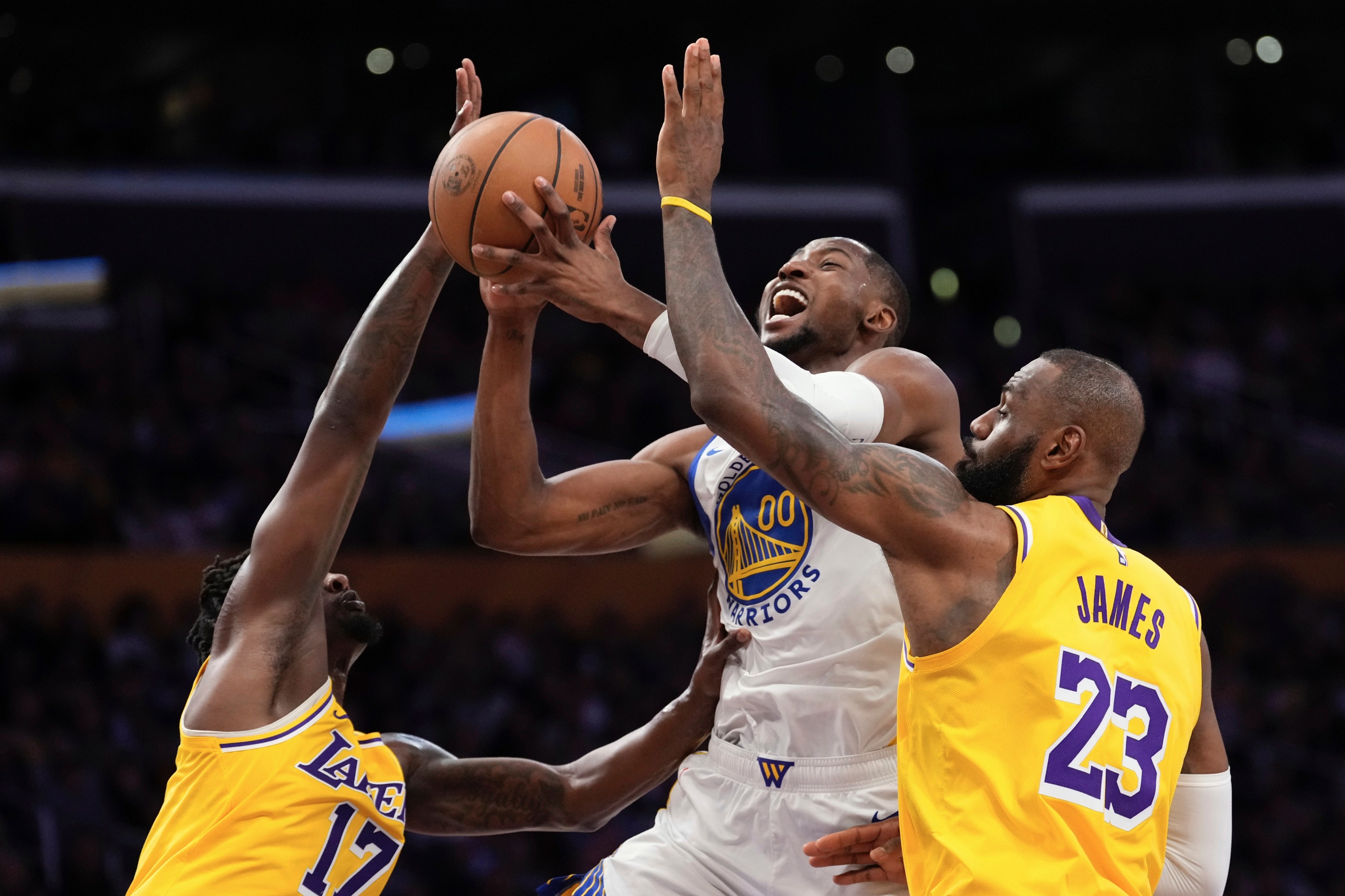 Two basketball players in yellow jerseys and one in a white jersey are fighting for possession of the ball during an intense game moment.