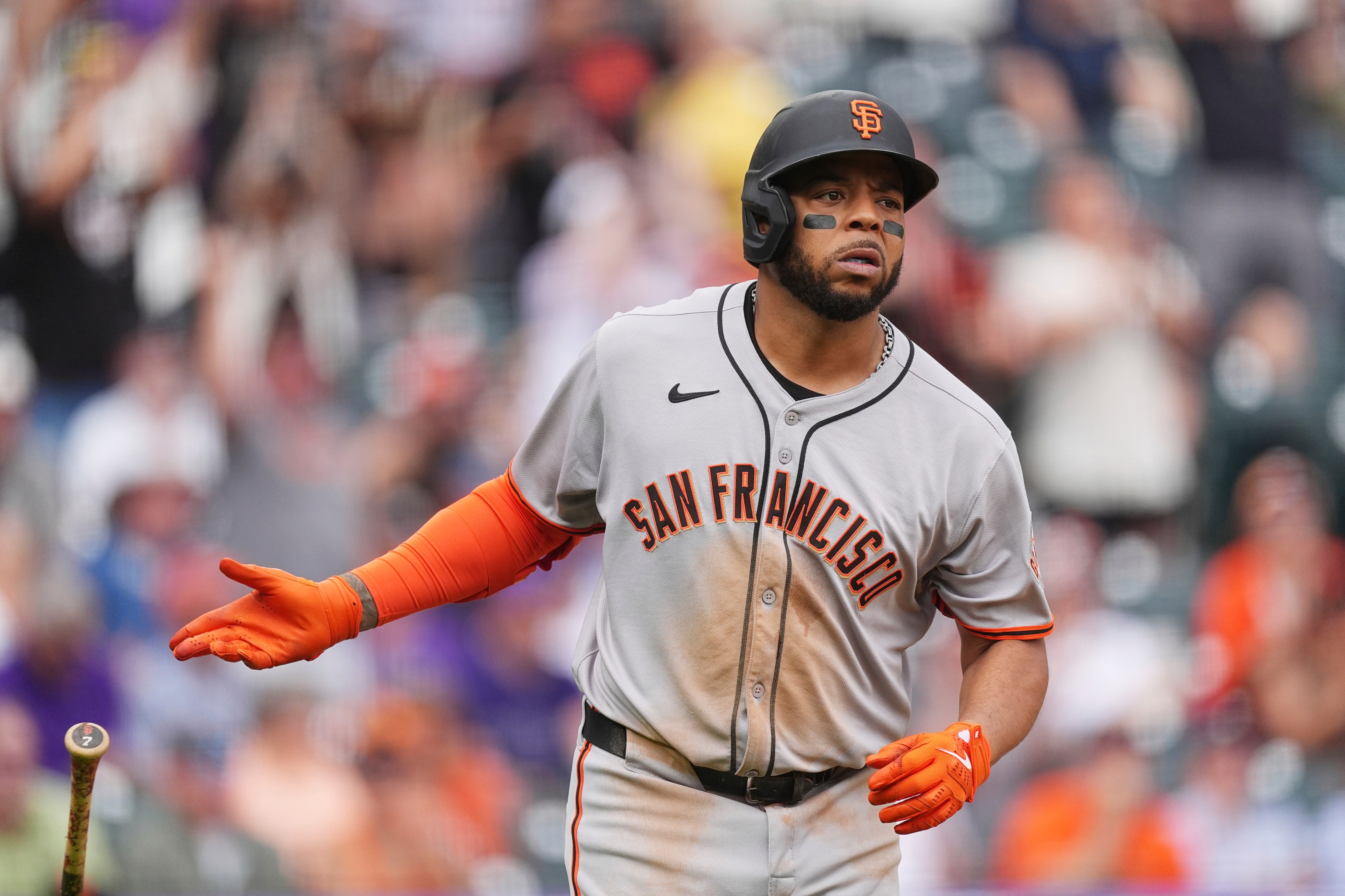A baseball player in a San Francisco Giants uniform swings a bat. He wears orange batting gloves and a helmet, with eye black applied to his face.