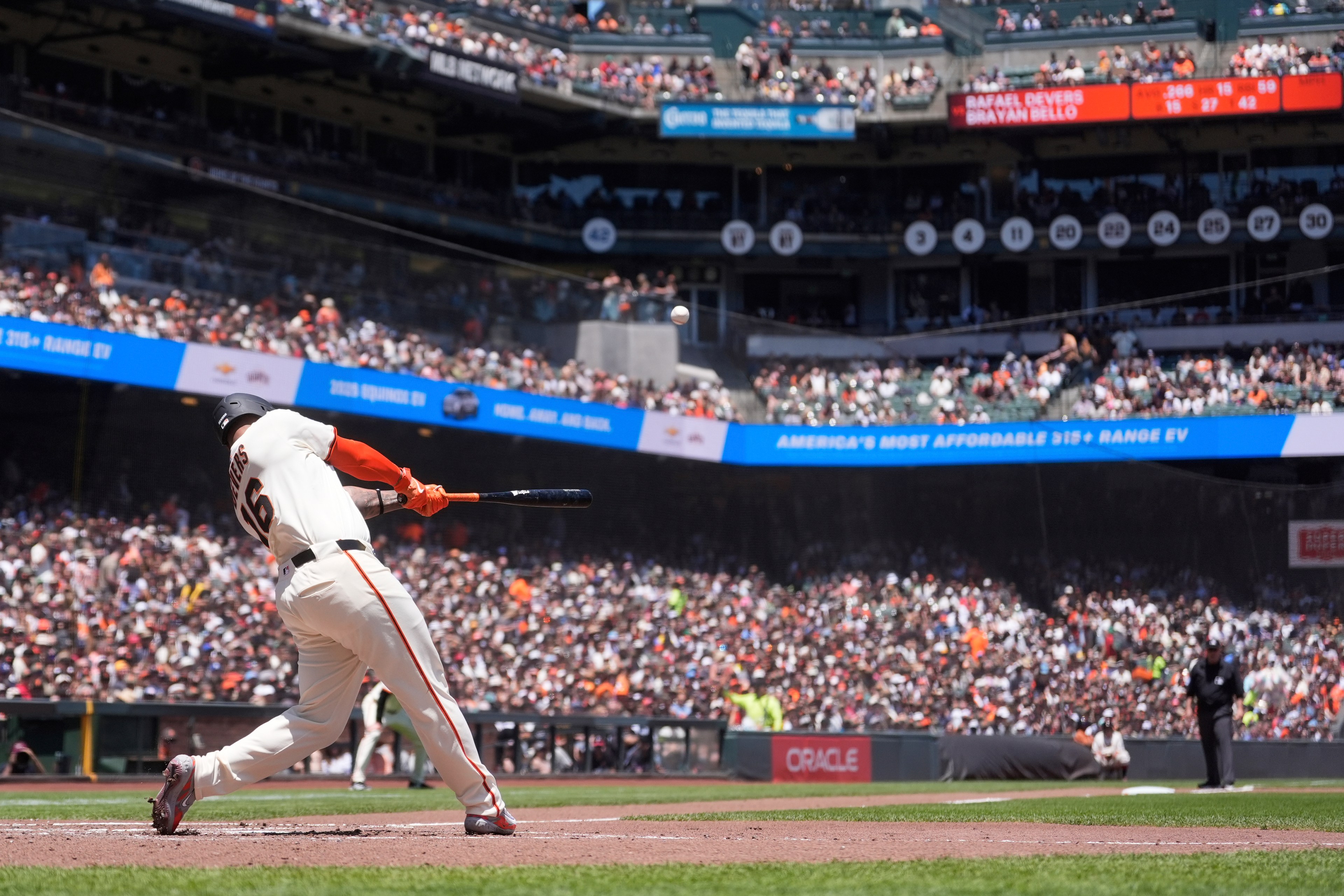 A baseball player in a white uniform with number 66 is mid-swing in a packed stadium. The crowd and scoreboards are visible in the background.