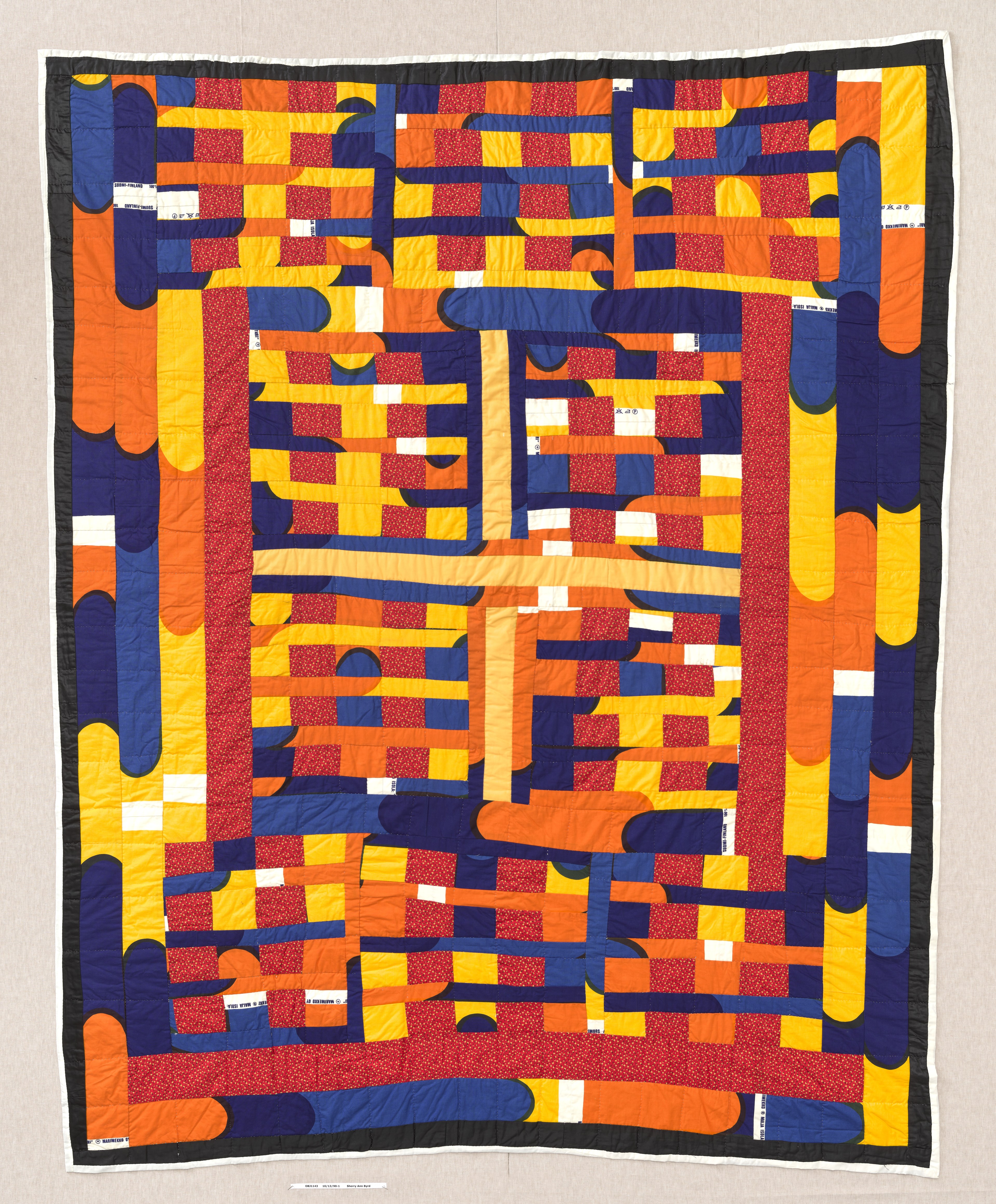 The image shows a vibrant quilt featuring geometric patterns with interlocking rectangles and curves in colors like orange, yellow, blue, and red.