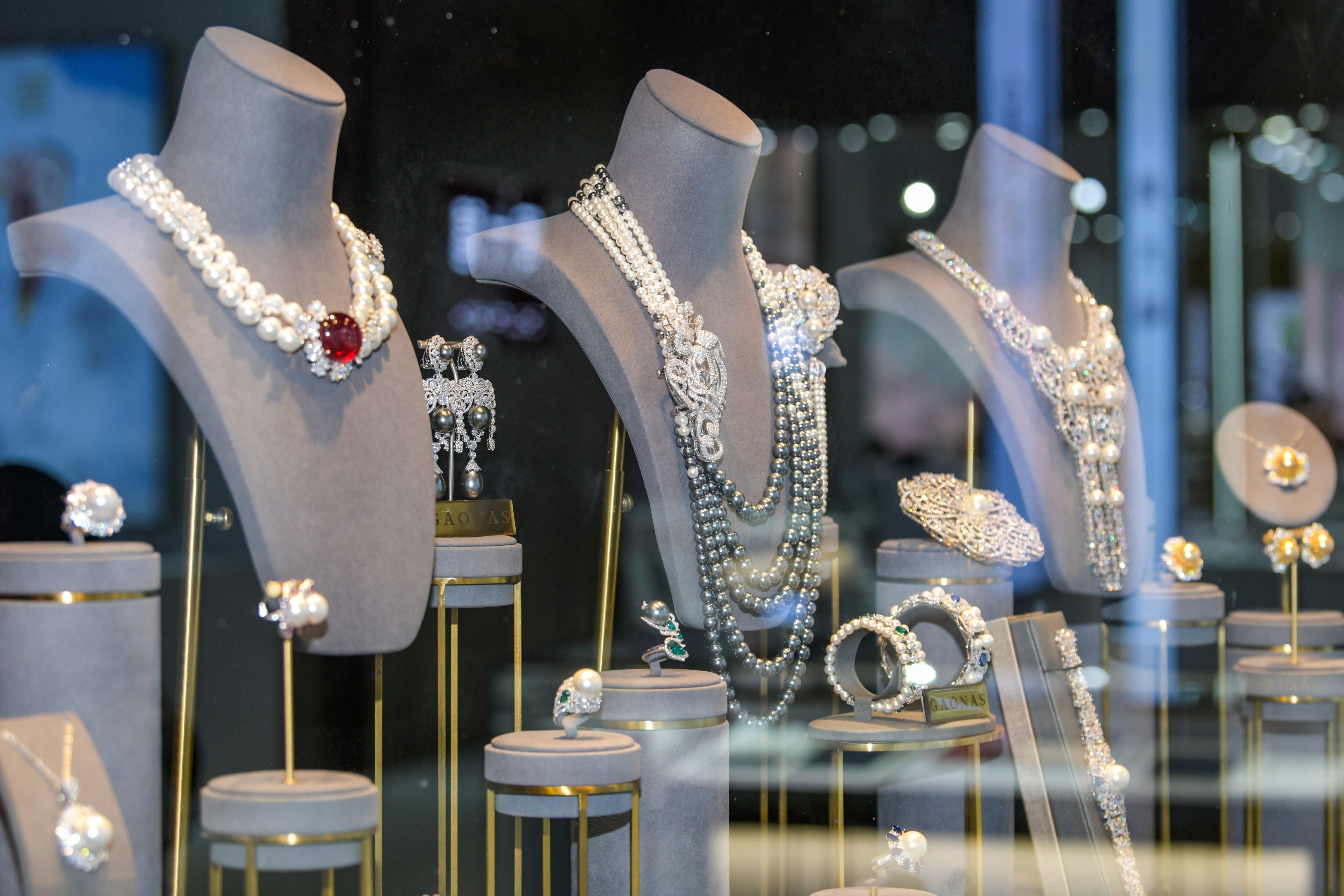 The image shows a jewelry store display with busts adorned with pearl necklaces, a large red jewel, intricate silver designs, and matching bracelets and rings.