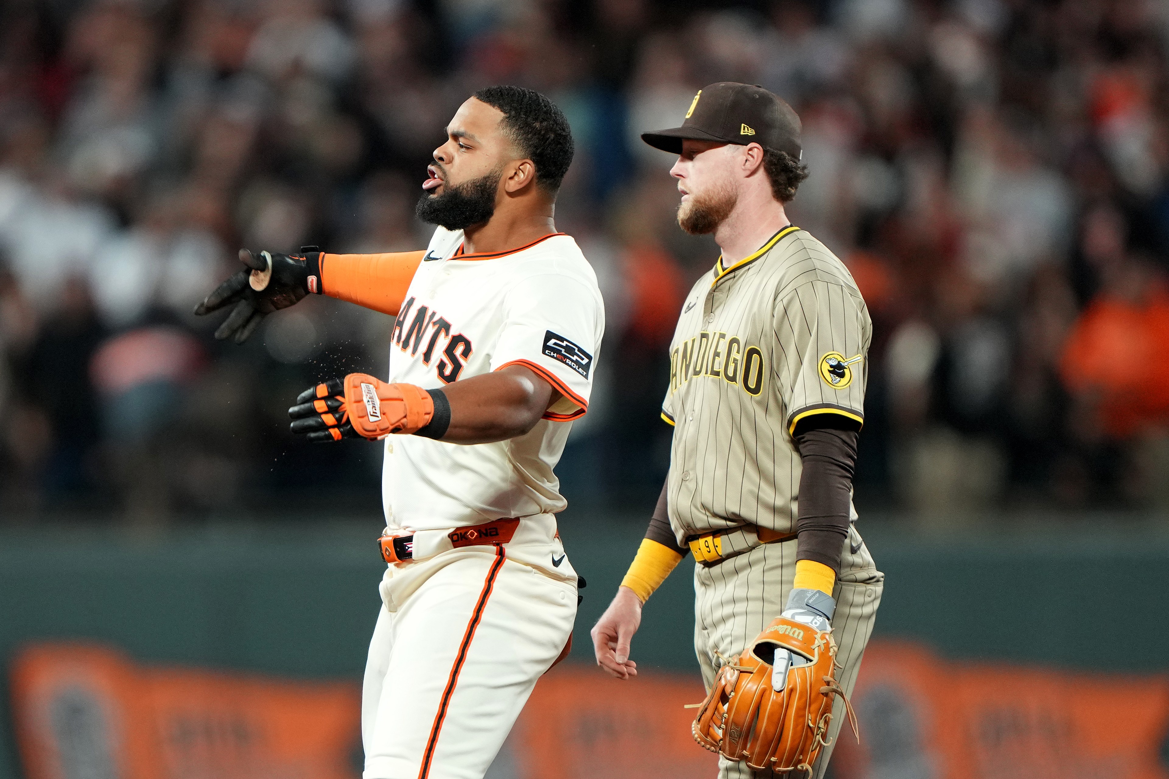 A baseball player in a white &quot;Giants&quot; uniform gestures passionately, while another in a striped &quot;San Diego&quot; uniform and cap stands beside him holding a glove.
