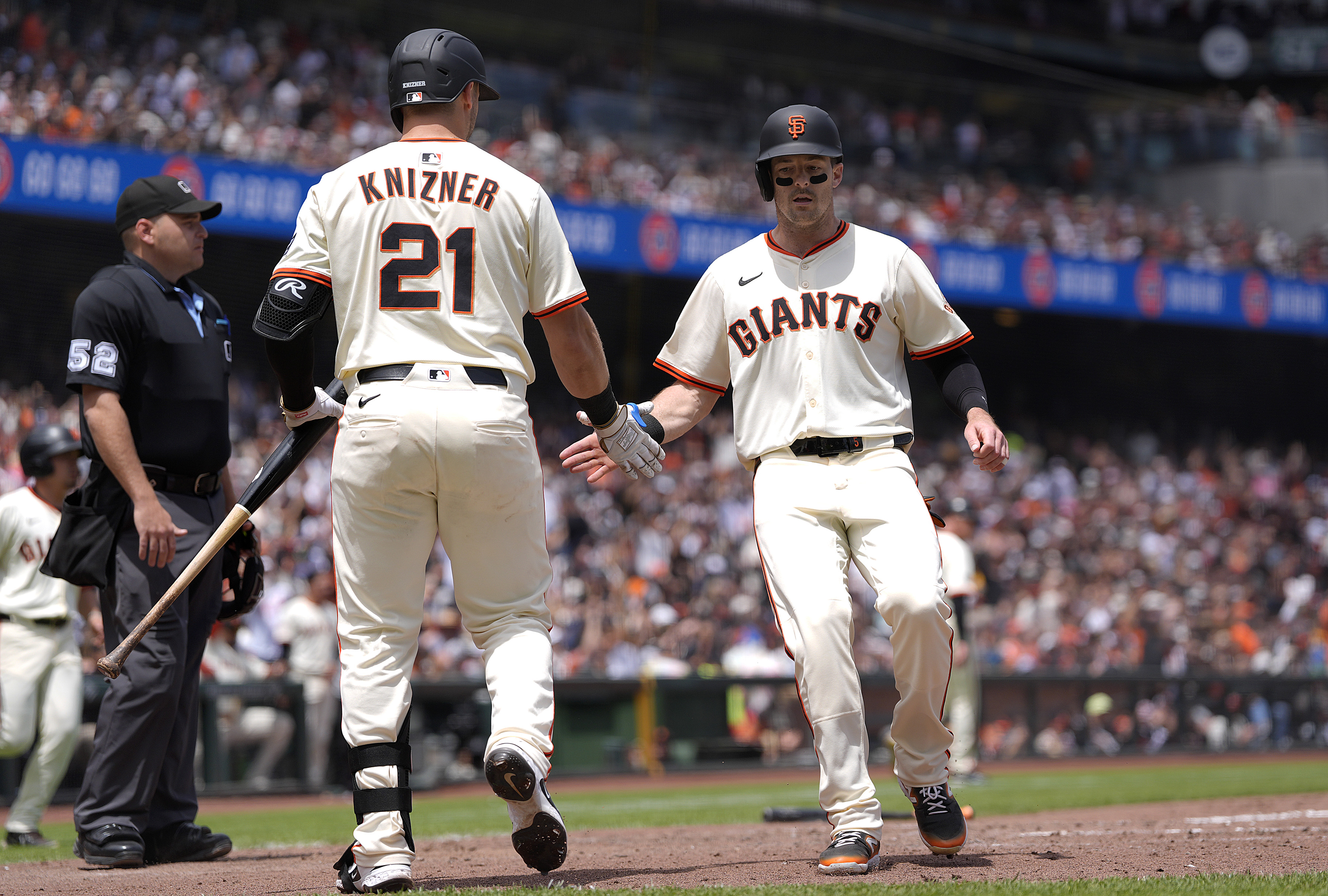 Two baseball players in white uniforms, one labeled &quot;Knizner,&quot; high-five near an umpire during a game. A crowd fills the stadium in the background.