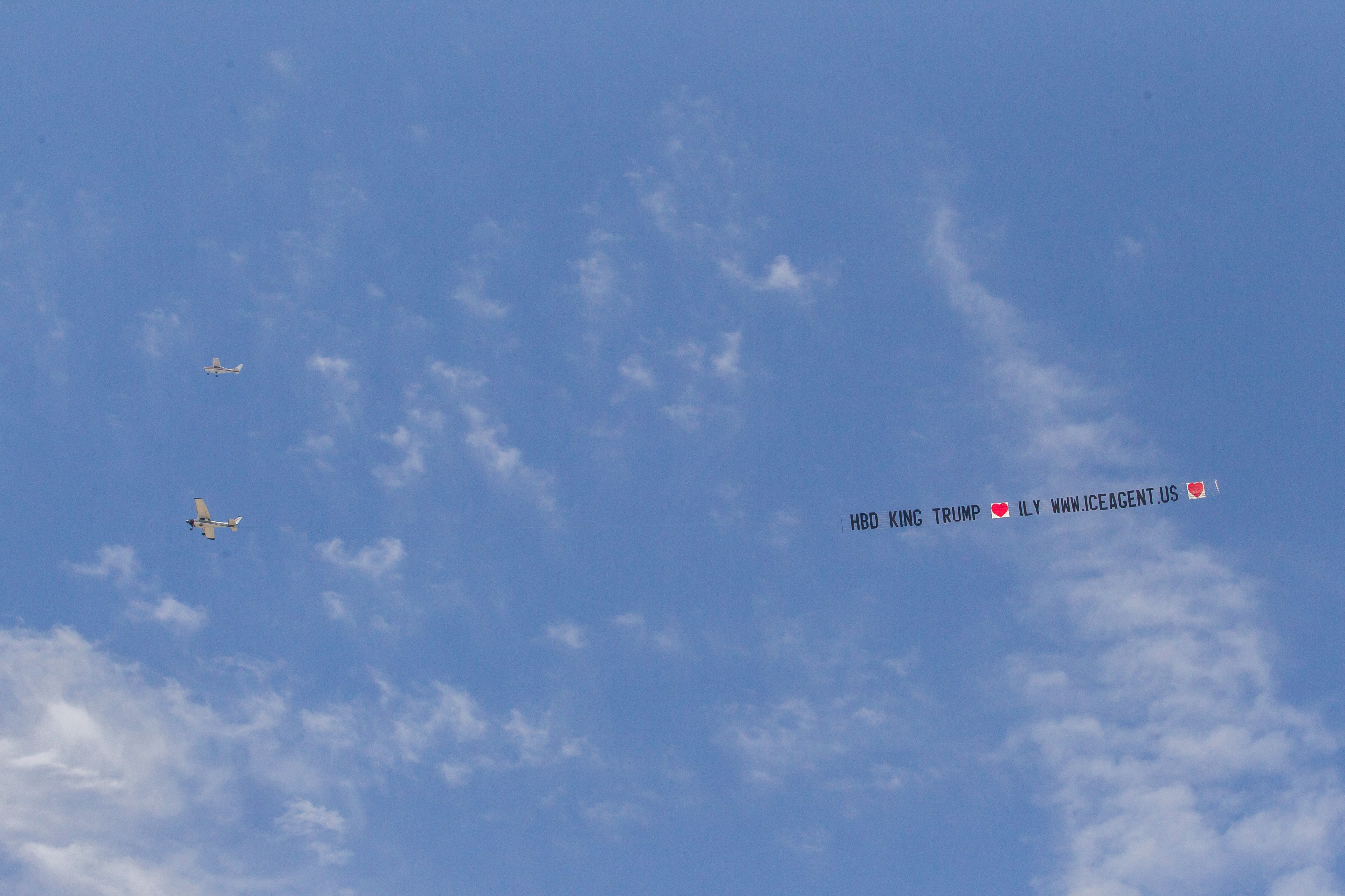 A small plane flies in the sky towing an ad that reads: &quot;HBD King Trump ILY www.iceagents.us&quot;