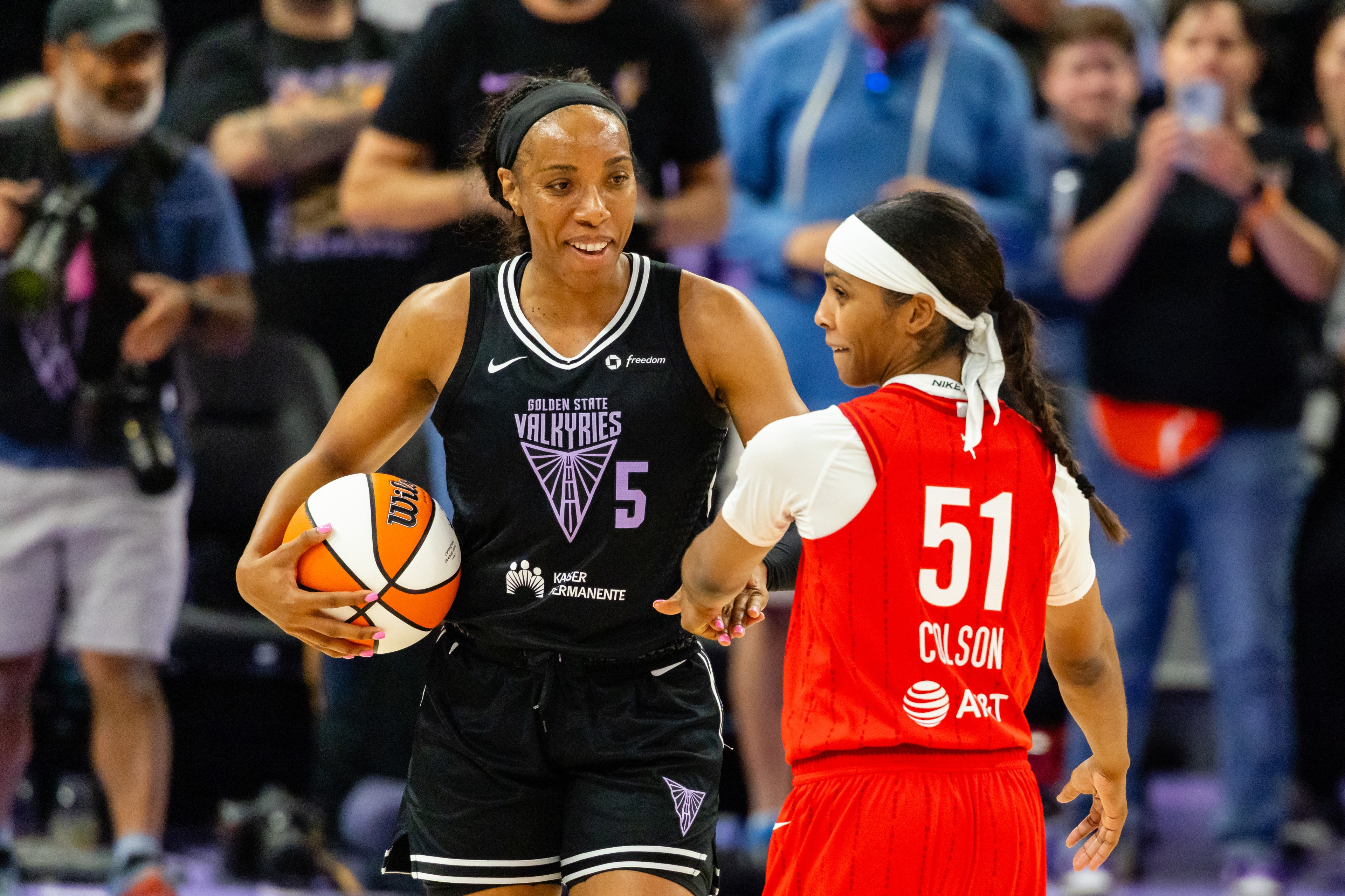 Two women are playing basketball; one in a black "Golden State Valkyries" jersey with number 5 is holding the ball, and the other in a red jersey with number 51 is nearby.