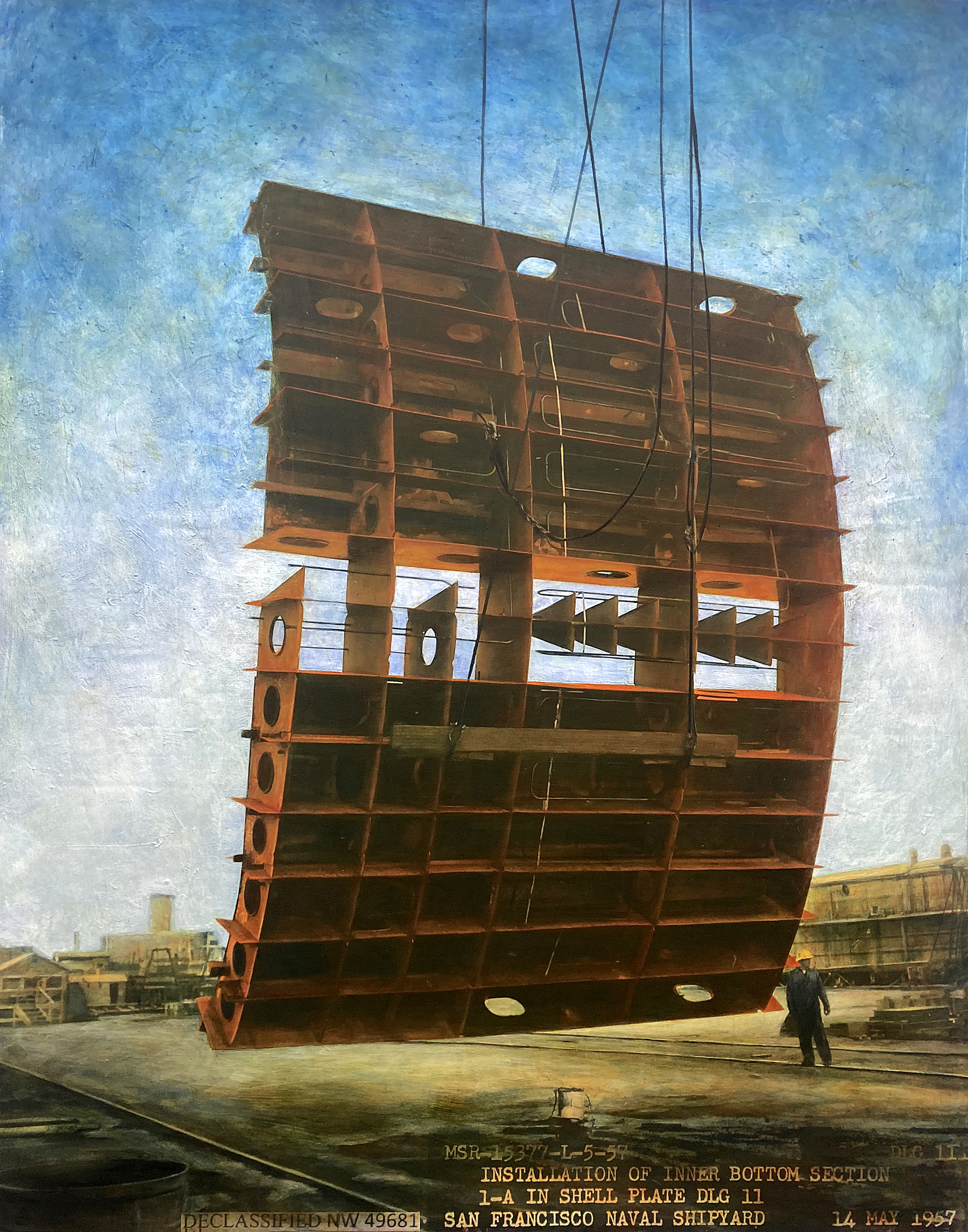 A large ship section is hoisted by cables at a shipyard. It's being installed, with a worker nearby for scale. The scene is set against a blue sky.